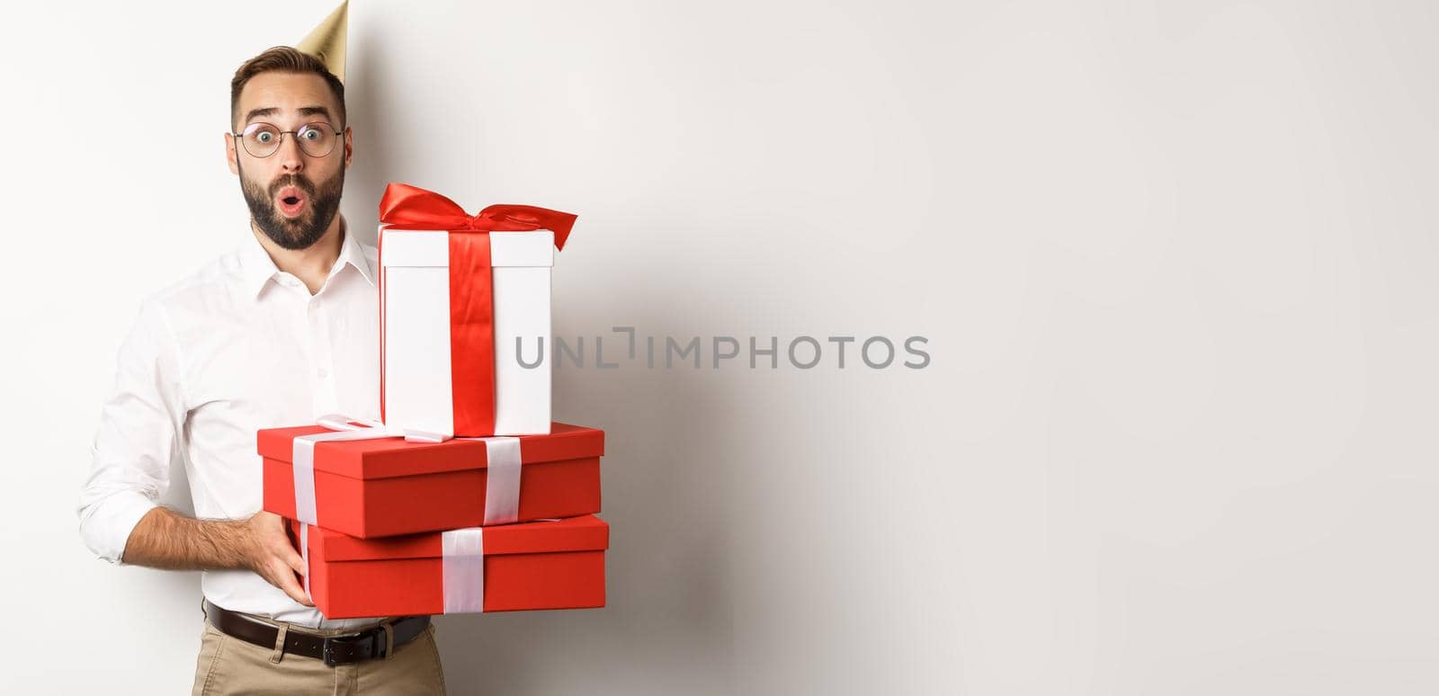 Holidays and celebration. Happy man receiving gifts on birthday, holding presents and looking excited, standing over white background.