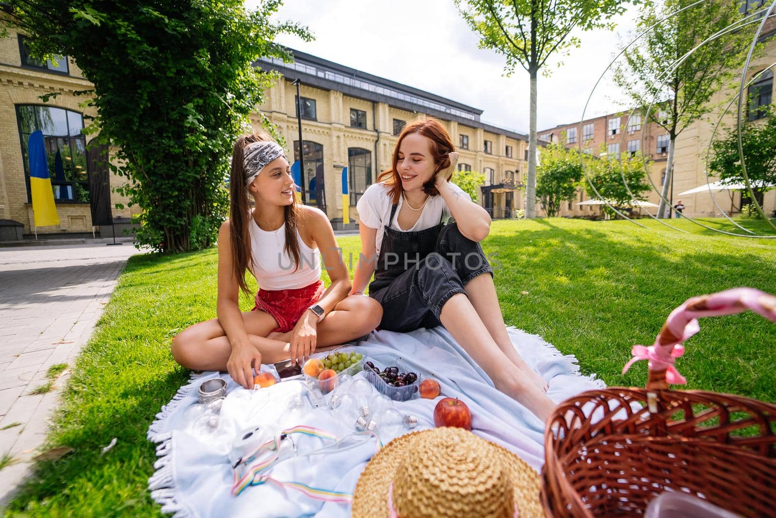 Two women having picnic together, sitting on the plaid on the lawn