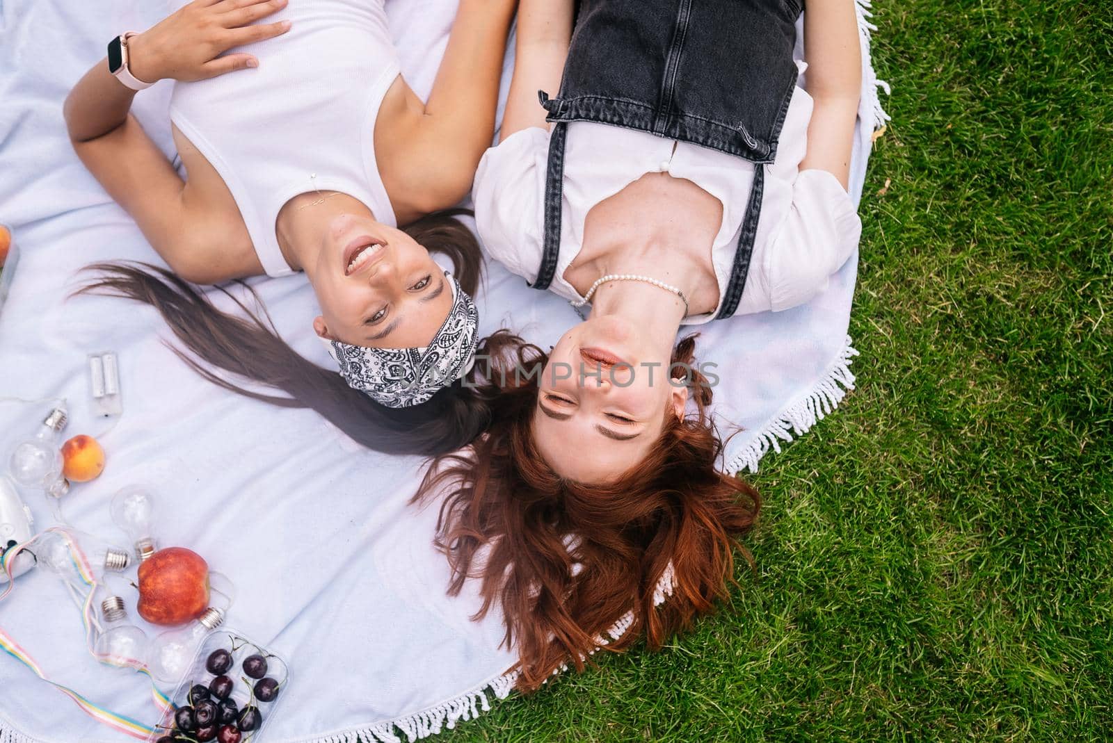 Two women having picnic together, laying on the plaid on the lawn