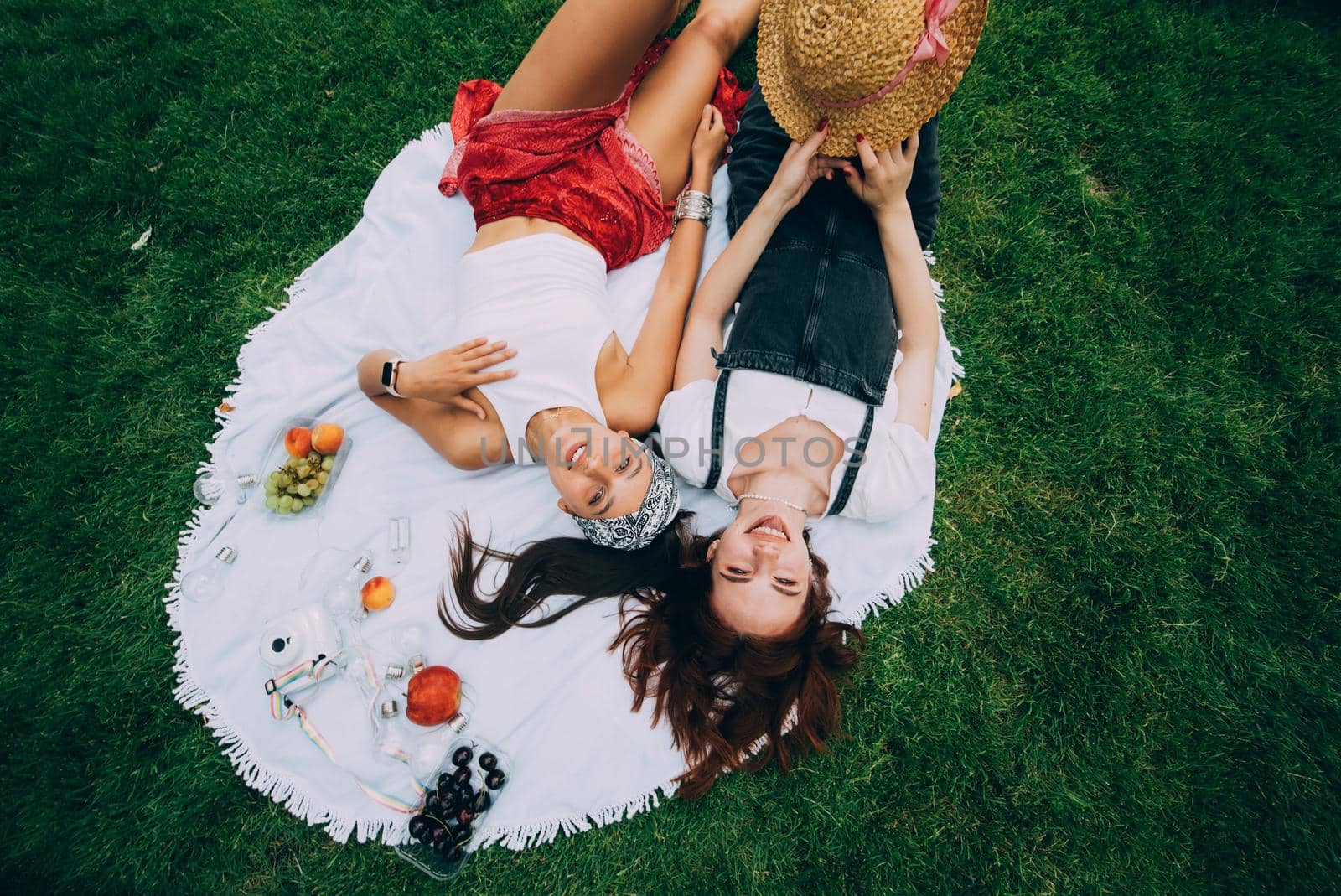 Two women having picnic together, laying on the plaid on the lawn