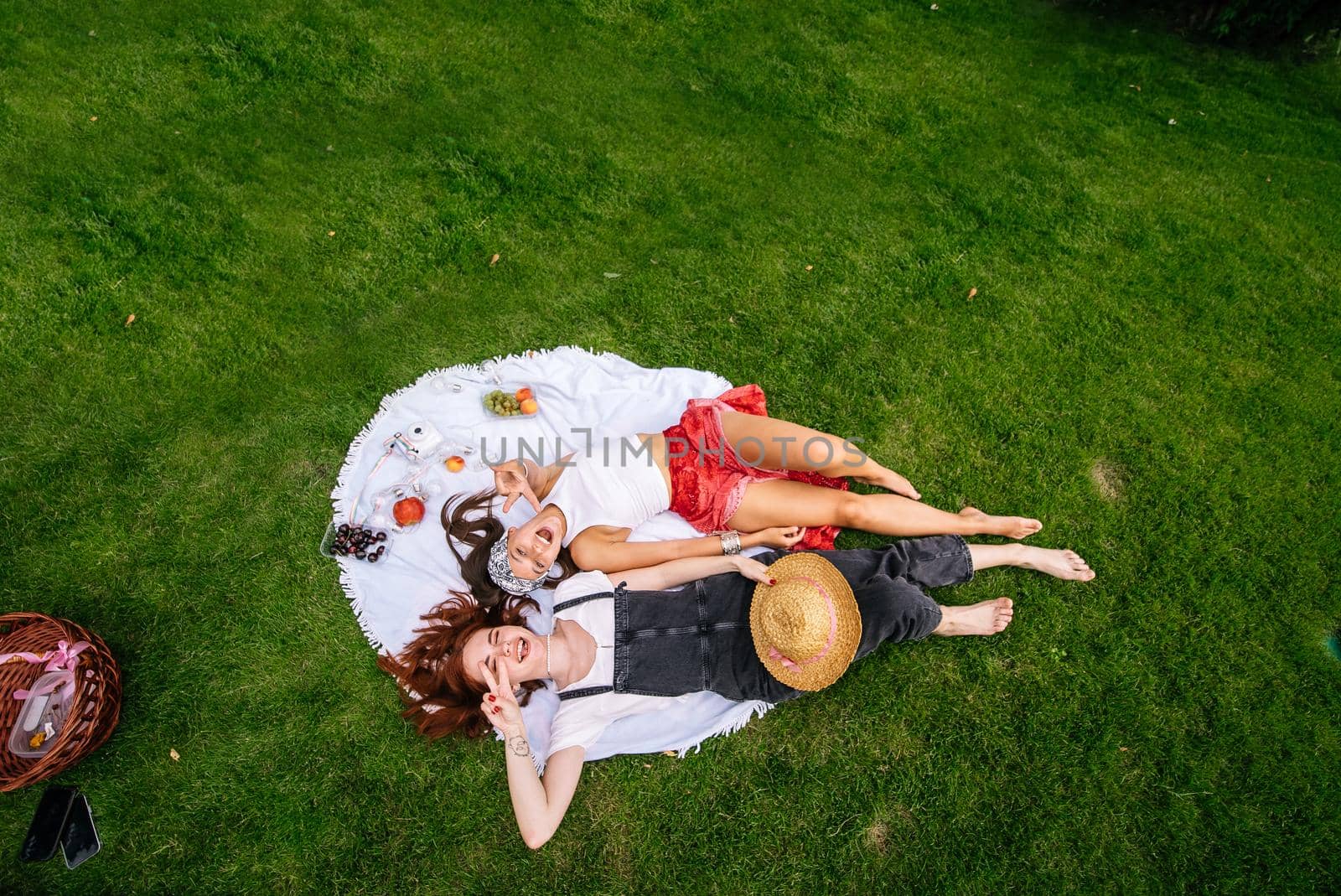 Two women having picnic together, laying on the plaid on the lawn