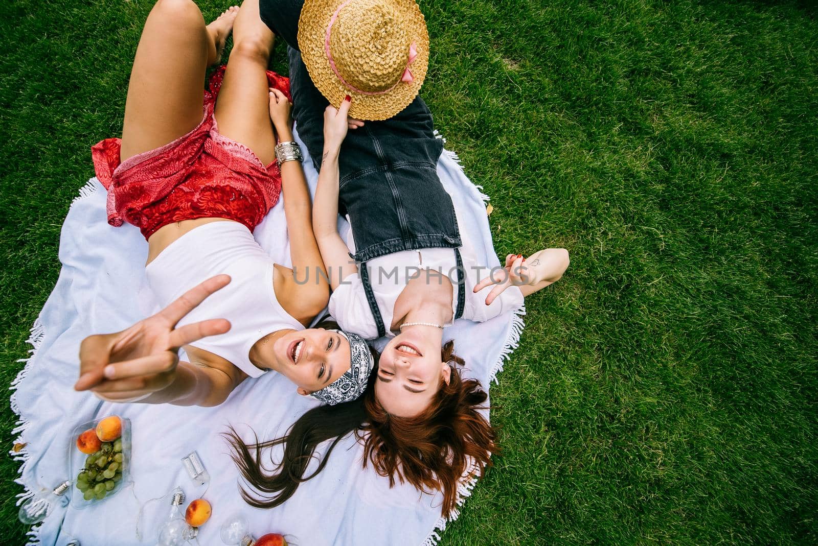 Two women having picnic together, laying on the plaid on the lawn