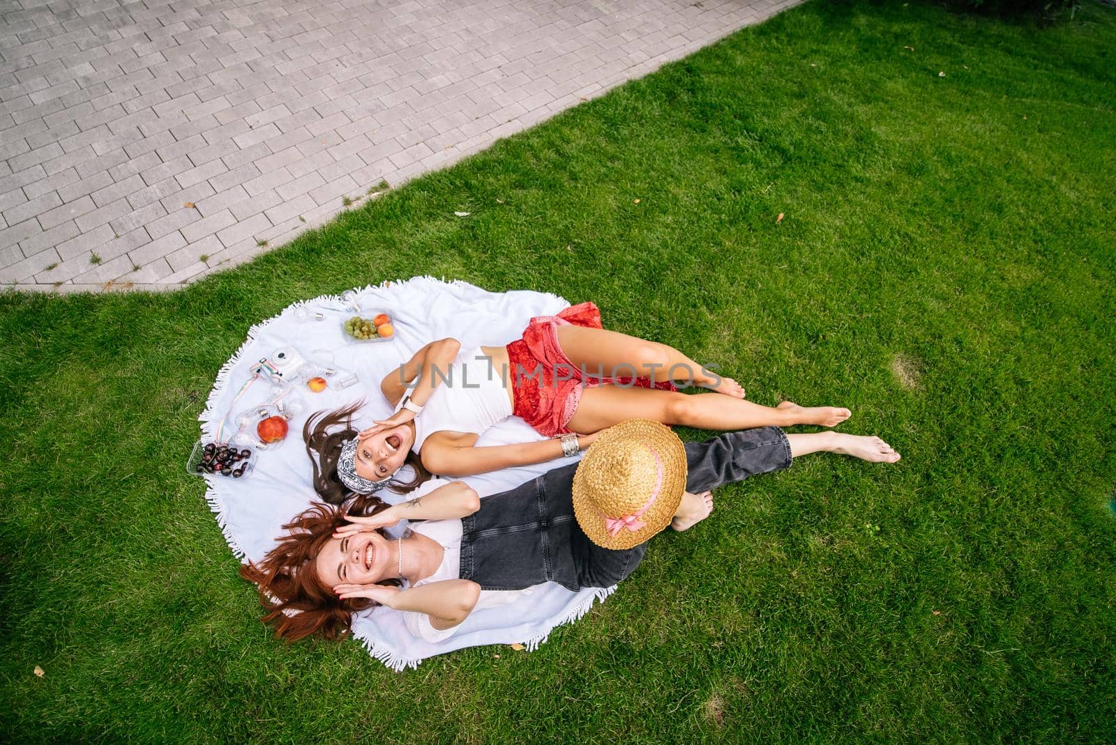 Two women having picnic together, laying on the plaid on the lawn