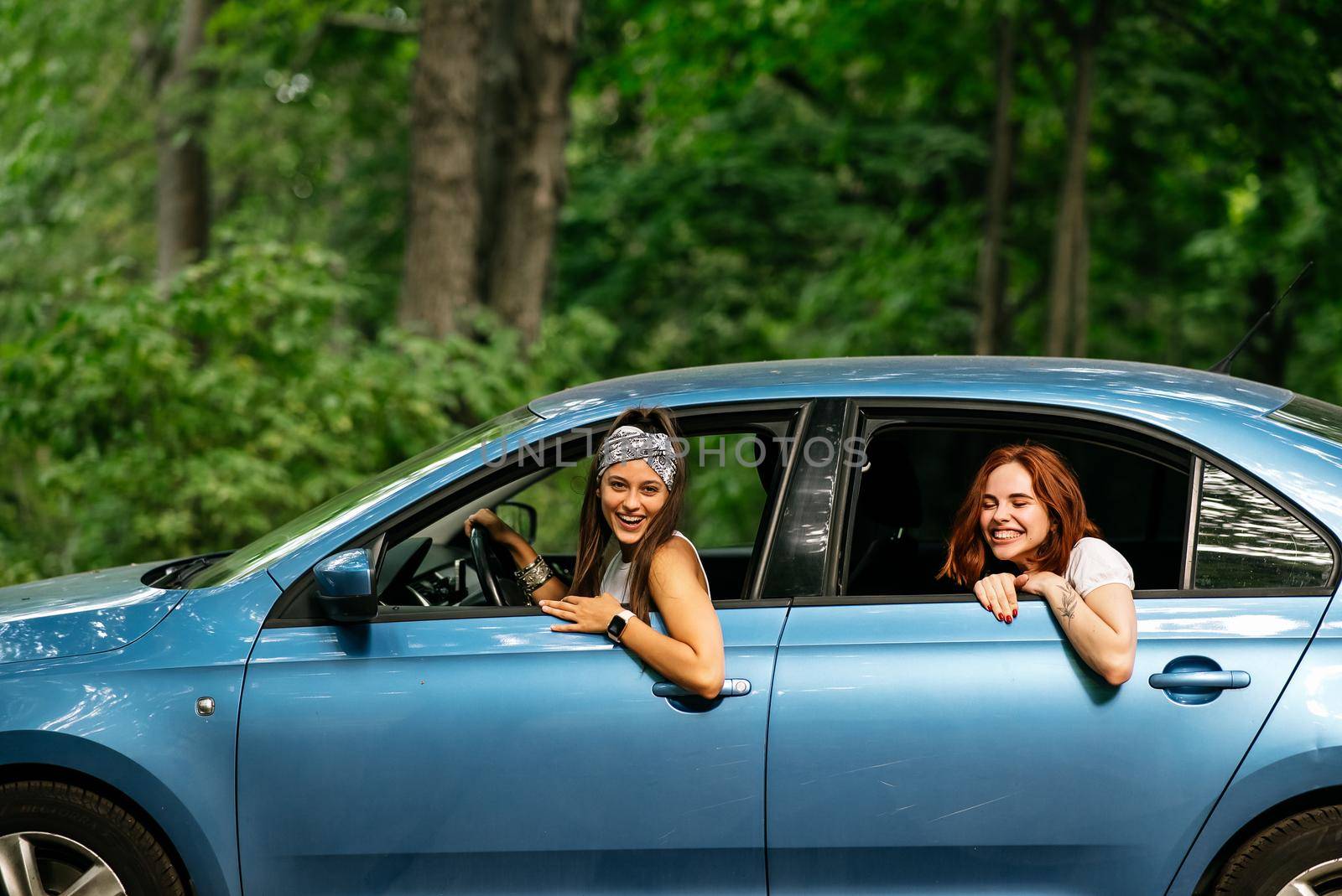 Two attractive young girlfriends fool around and laughing together in a car on a sunny day.