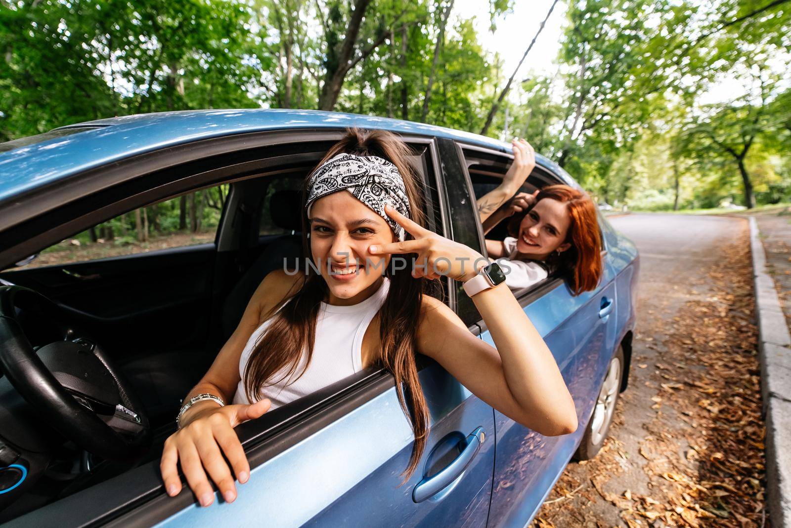 Two attractive young girlfriends fool around and laughing together in a car on a sunny day.