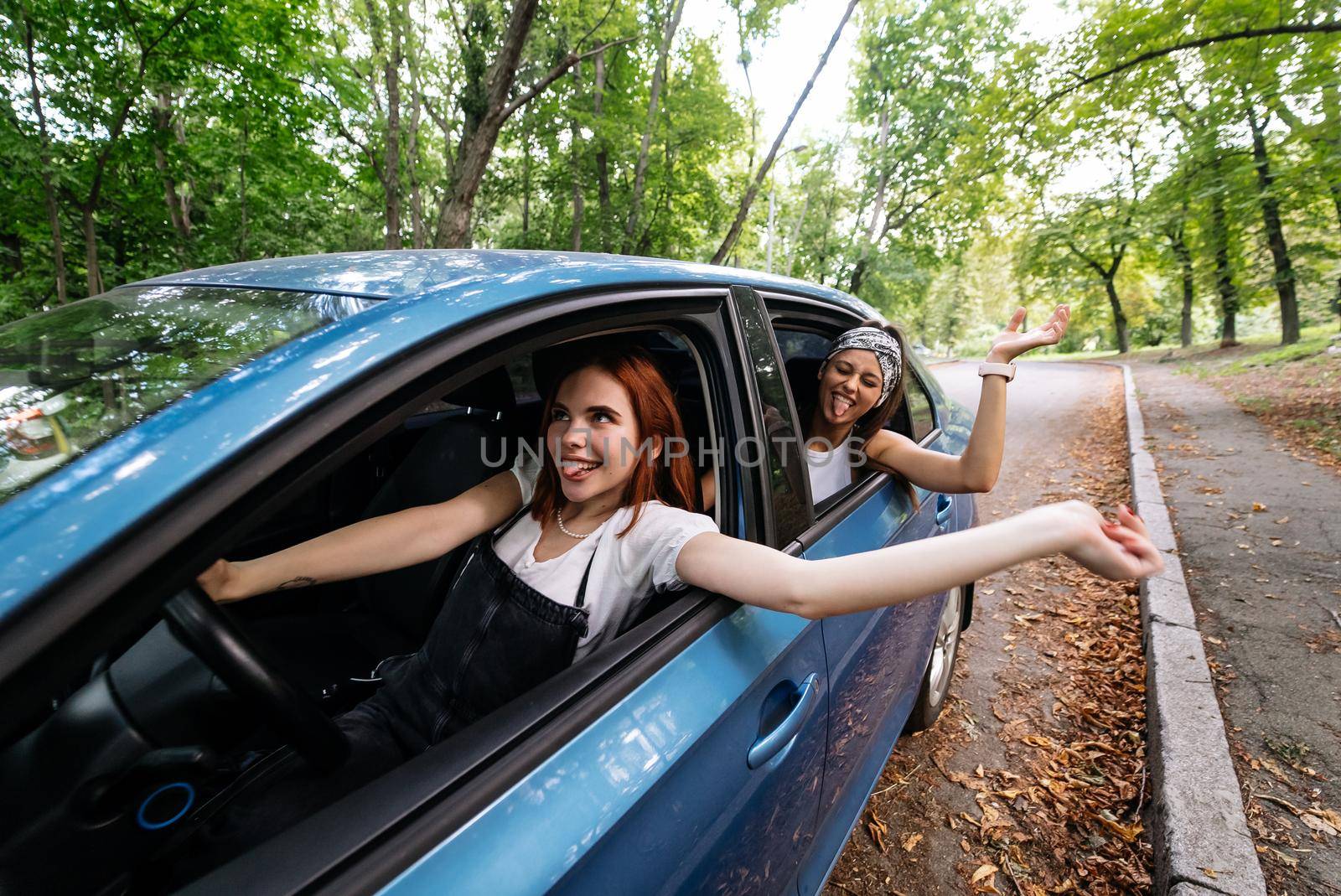 Two attractive young girlfriends fool around and laughing together in a car on a sunny day.