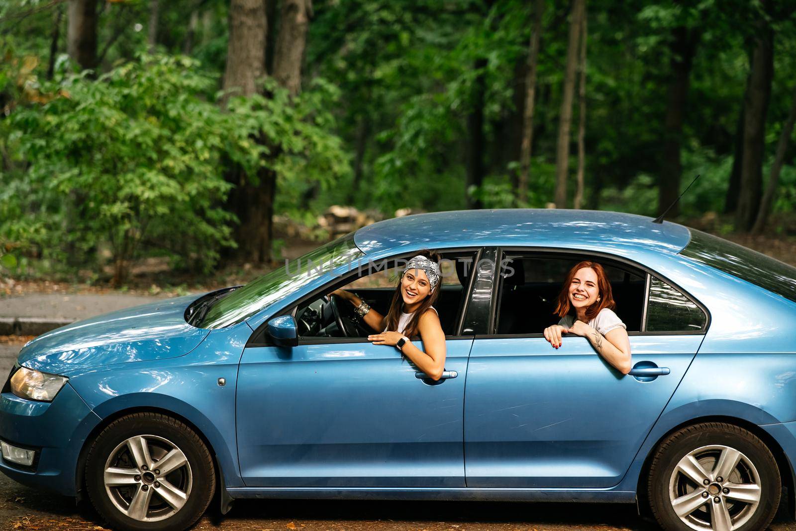 Two attractive young girlfriends fool around and laughing together in a car on a sunny day.