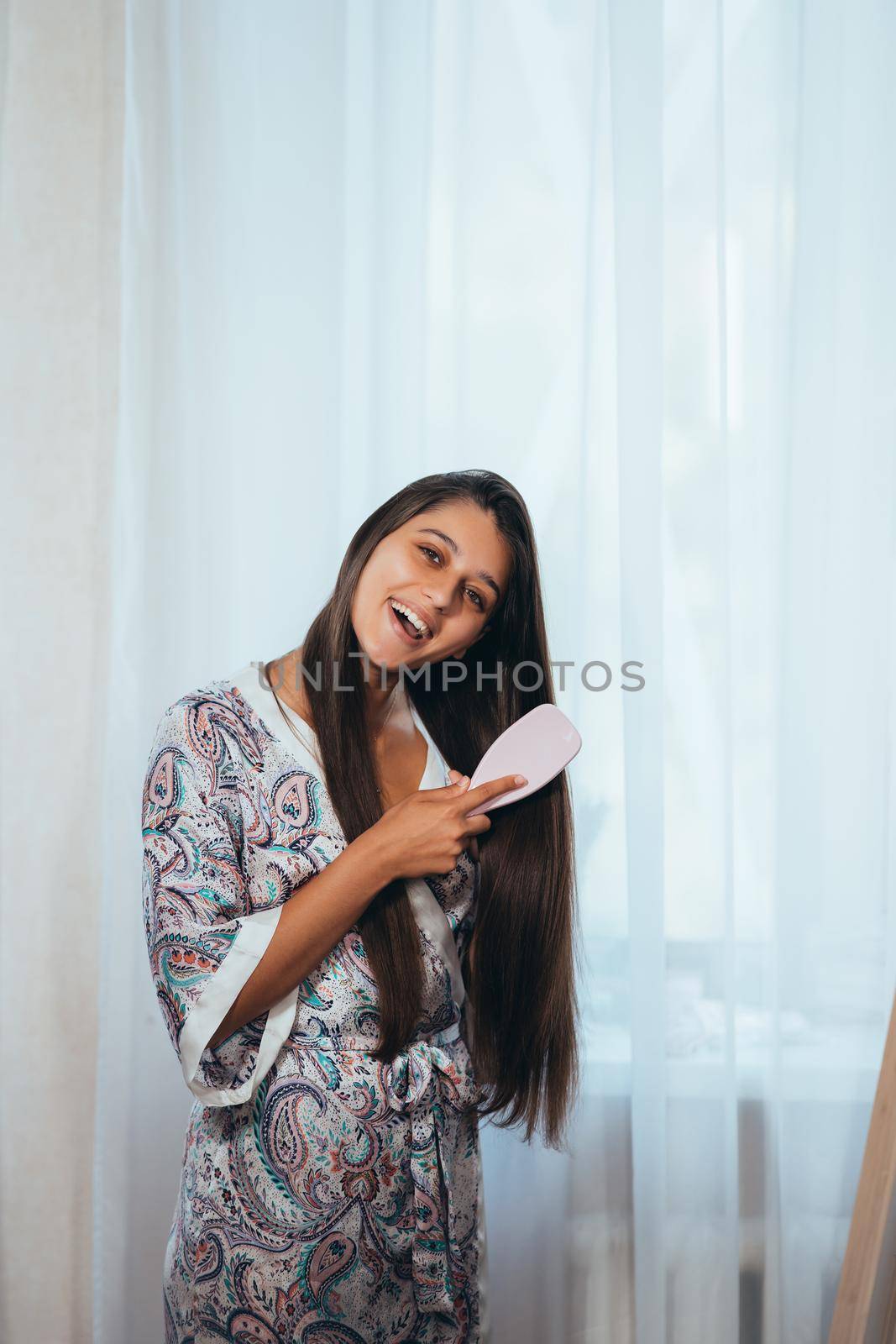 Beautiful young woman combing hair at baedroom by teksomolika