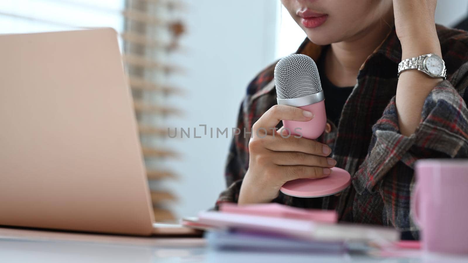 Cropped image of female radio host speaking in microphone and using laptop for making audio podcast.