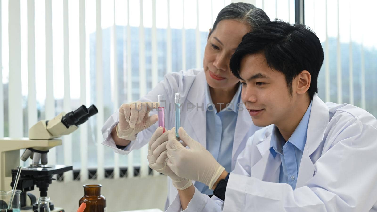 Senior scientist and laboratory assistant discussing about new test results in laboratory. Science research and people concept.