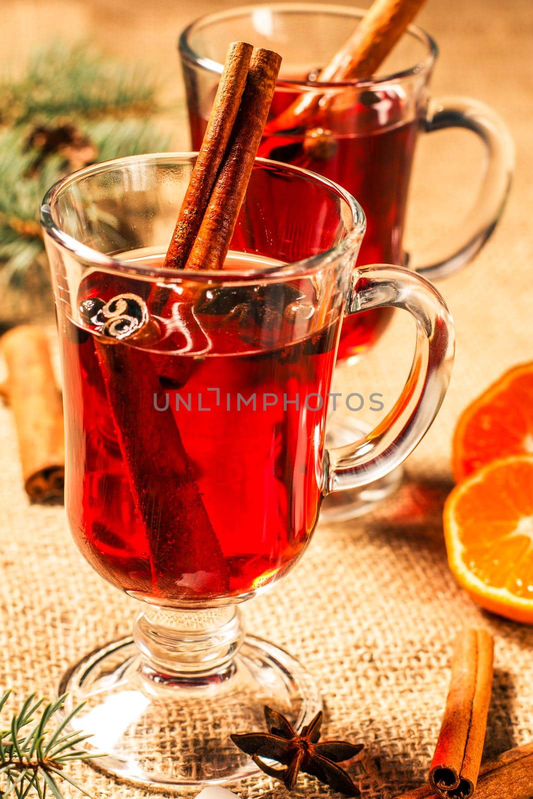 Glass of Christmas mulled wine with cinnamon, star anise and cloves on sackcloth with slices of orange, natural fir tree branches and cones. Color toning effect.