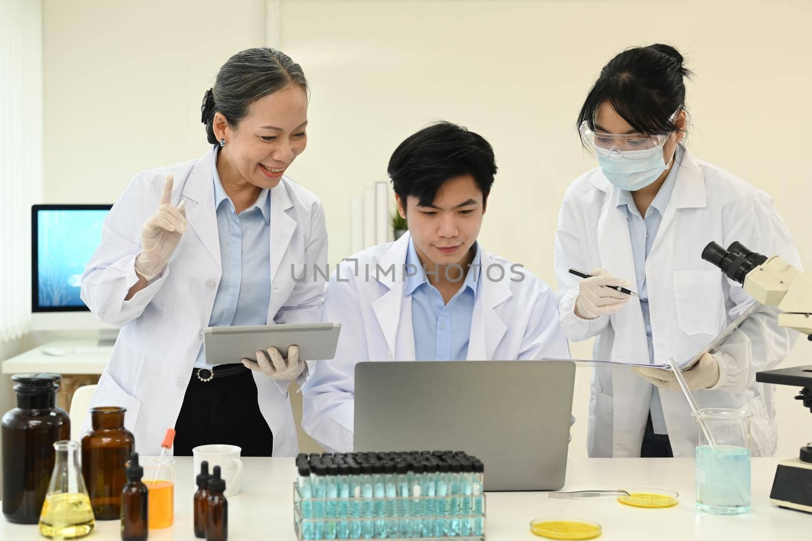 Professional scientist team looking at laptop screen, collecting data and summarising information for scientific report.