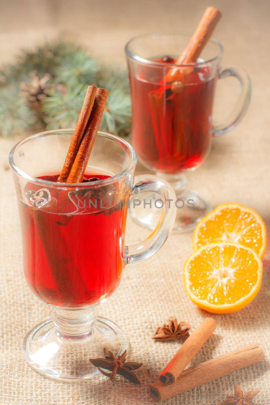 Glass of Christmas mulled wine with cinnamon, star anise and cloves on sackcloth with slices of orange, natural fir tree branches and cones. Color toning effect.