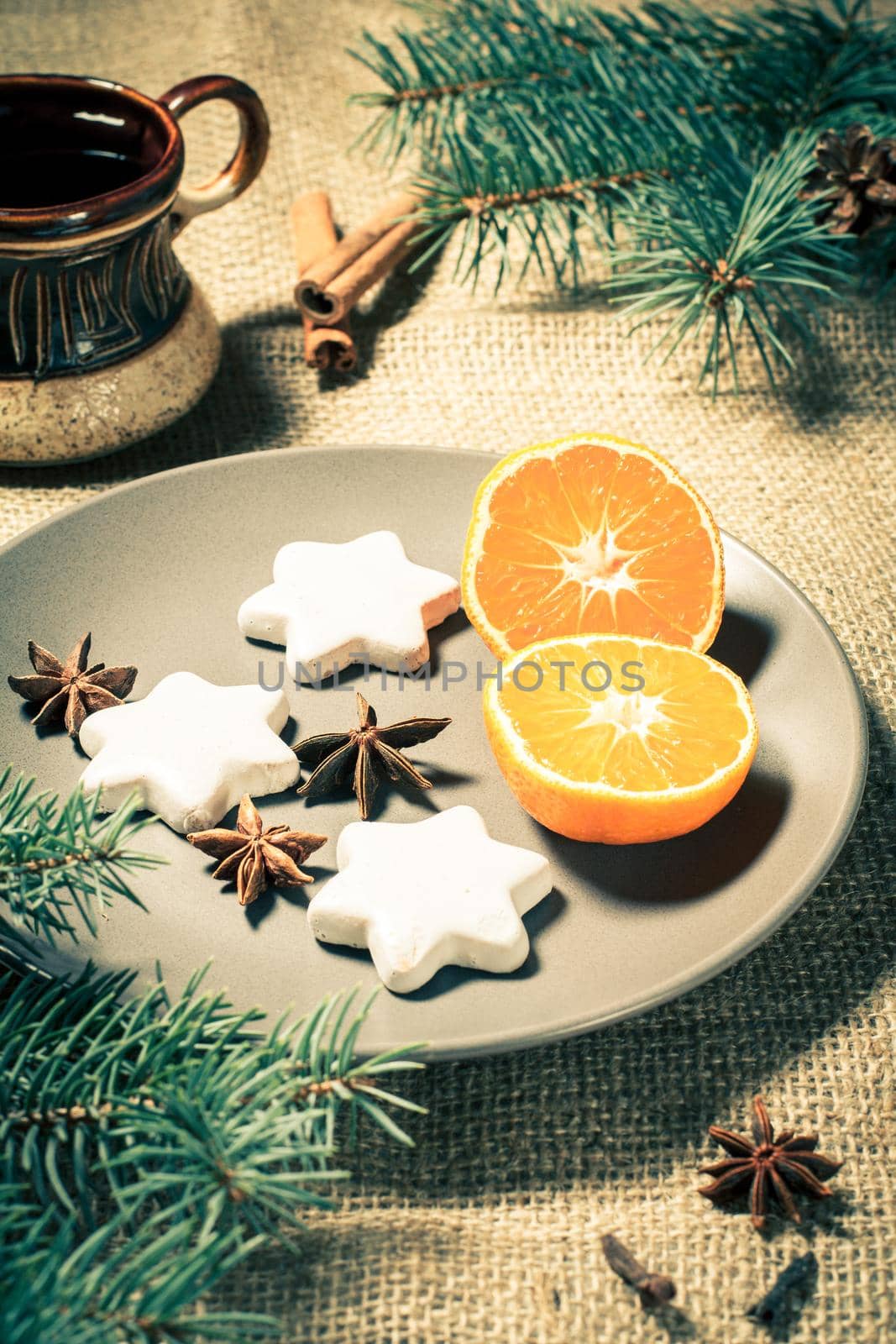 Gingerbread cookies in star shape on plate with cinnamon, star anise and natural fir tree branches with cones, cup of coffee on sackcloth. Color toning effect.