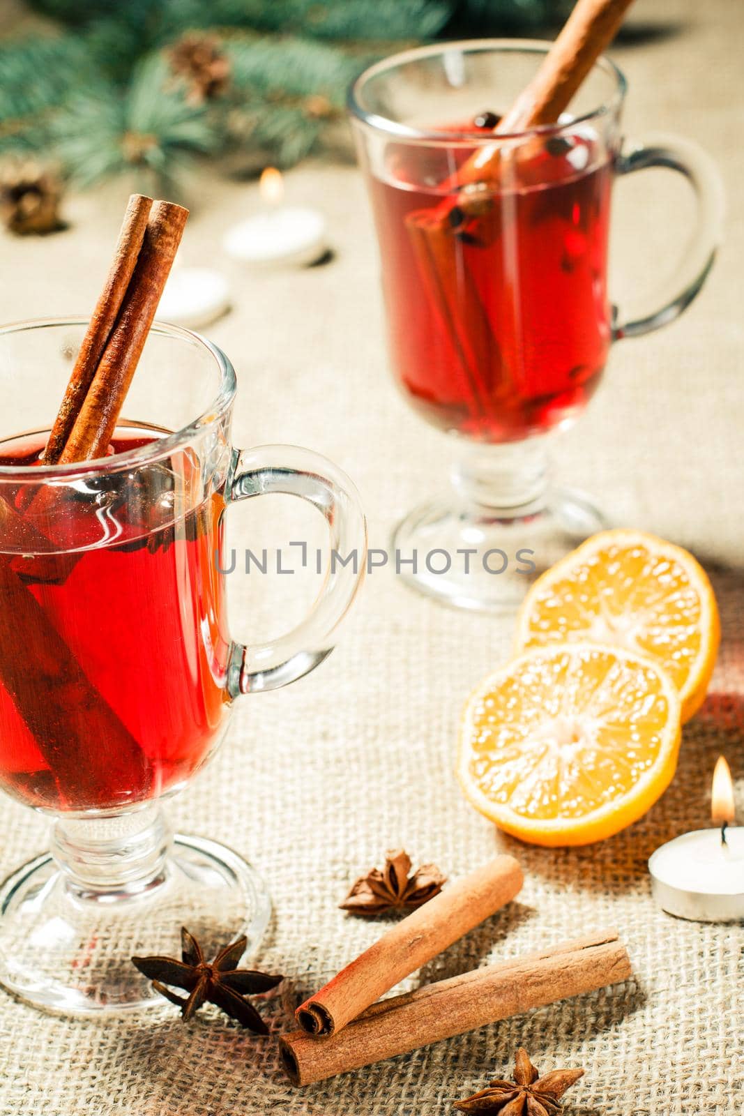 Glass of Christmas mulled wine with cinnamon, star anise and cloves on sackcloth with slices of orange, natural fir tree branches and cones. Color toning effect.