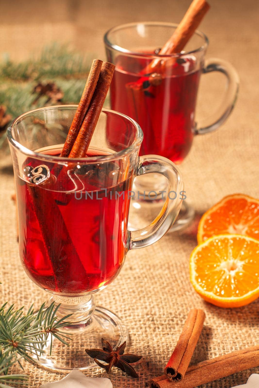 Glass of Christmas mulled wine with cinnamon, star anise and cloves on sackcloth with slices of orange, natural fir tree branches and cones. Color toning effect.