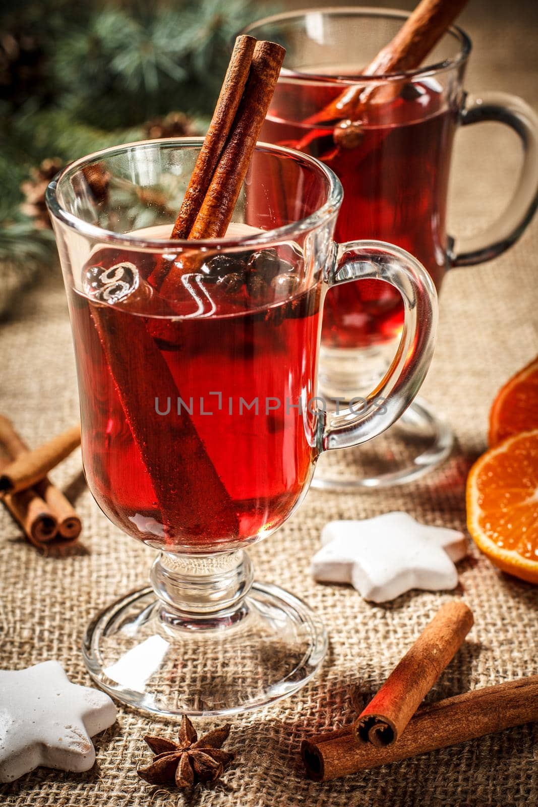 Glass of Christmas mulled wine with cinnamon, star anise and cloves on sackcloth with white biscuits, slices of orange, natural fir tree branches and cones. Color toning effect.