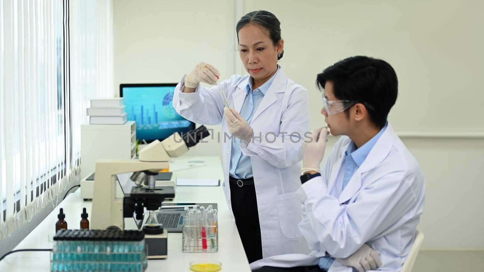 Two professional scientist conducting experiment with test tubes and microscope in research laboratory.