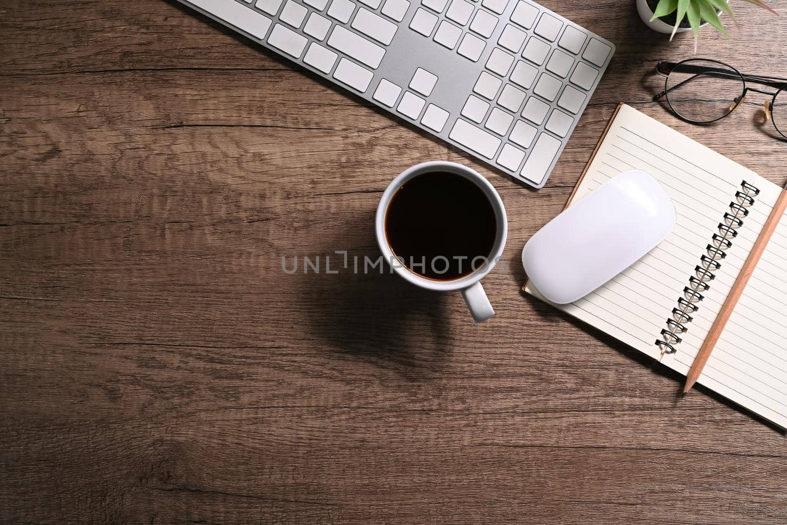 Top view wireless keyboard, cup of coffee and notebook on wooden background. Simple workplace.