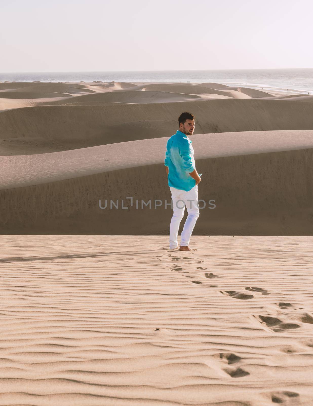 Young men walking at the beach of Maspalomas Gran Canaria Spain, men at the sand dunes desert by fokkebok