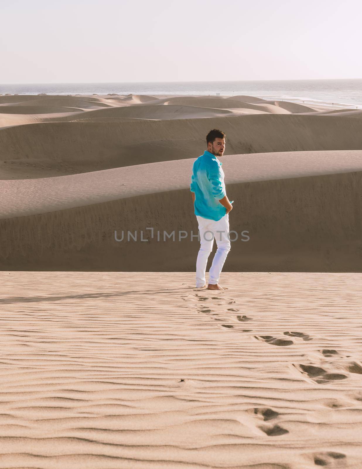 Young men walking at the beach of Maspalomas Gran Canaria Spain, men at the sand dunes desert of Maspalomas Gran Canaria during a vacation in Spain