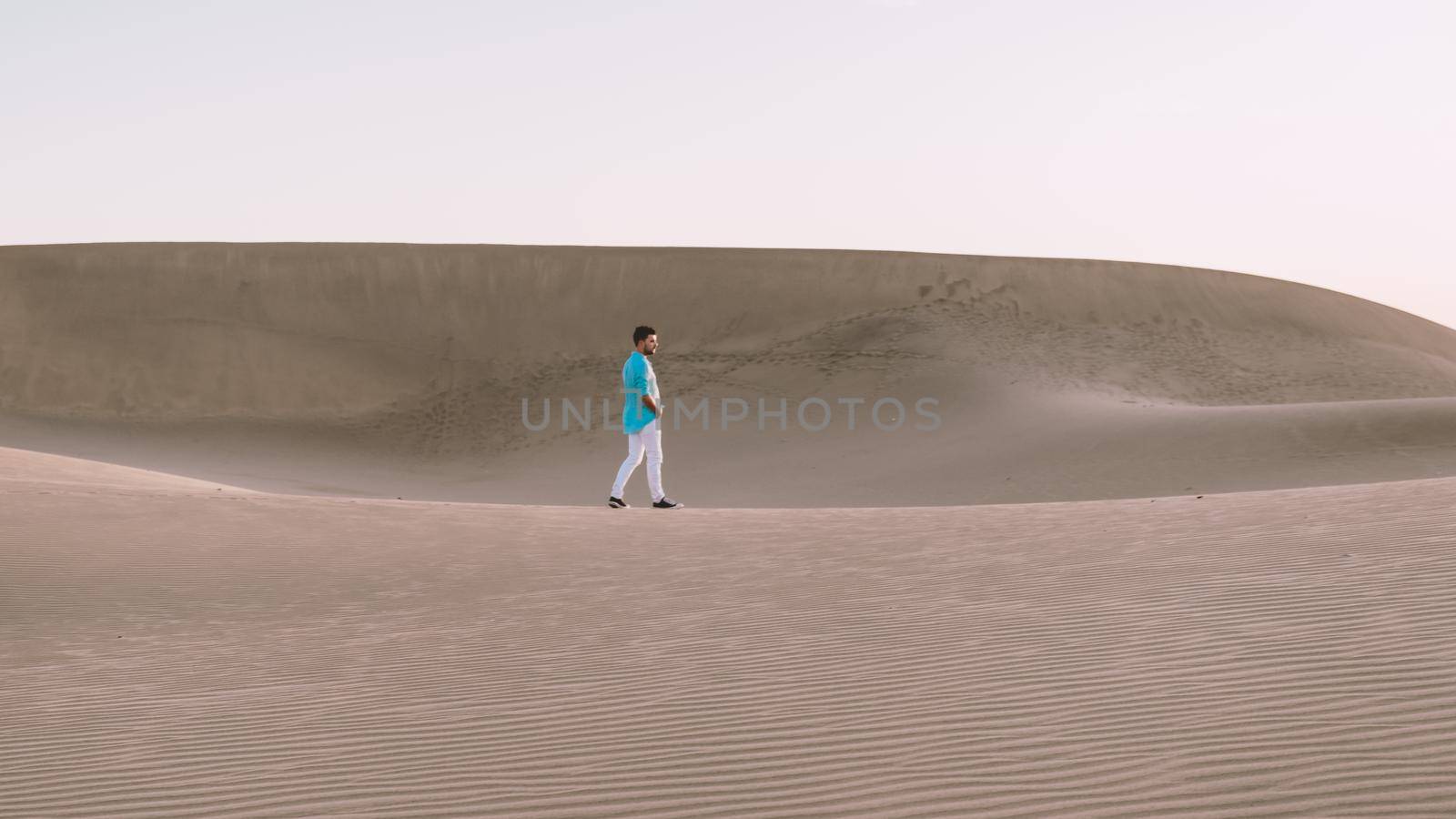 Young men walking at the beach of Maspalomas Gran Canaria Spain, young men walking in de sand during sun rise in the desert of Maspalomas Gran Canaria