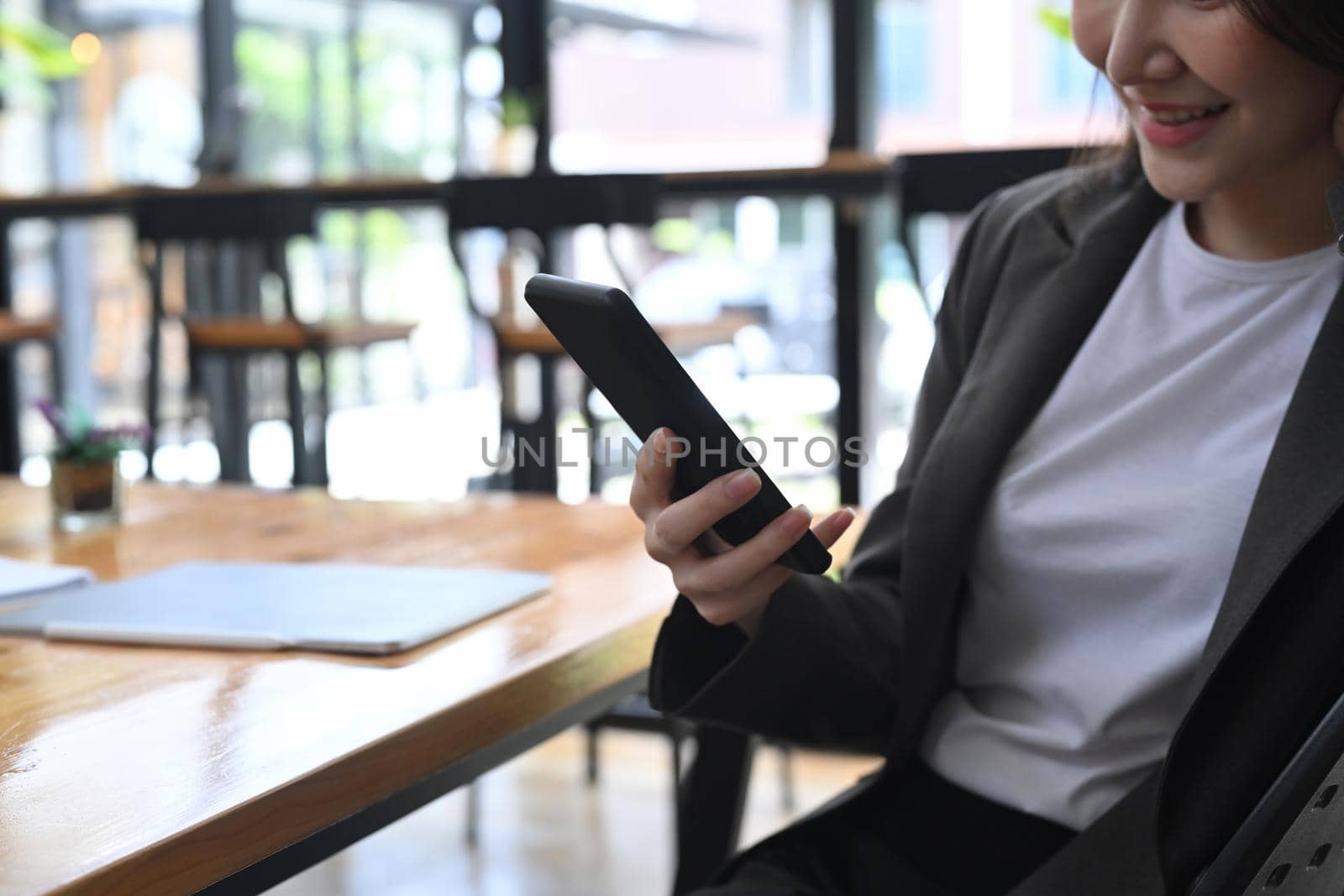 Smiling businesswoman sitting at her office desk and using smart phone.