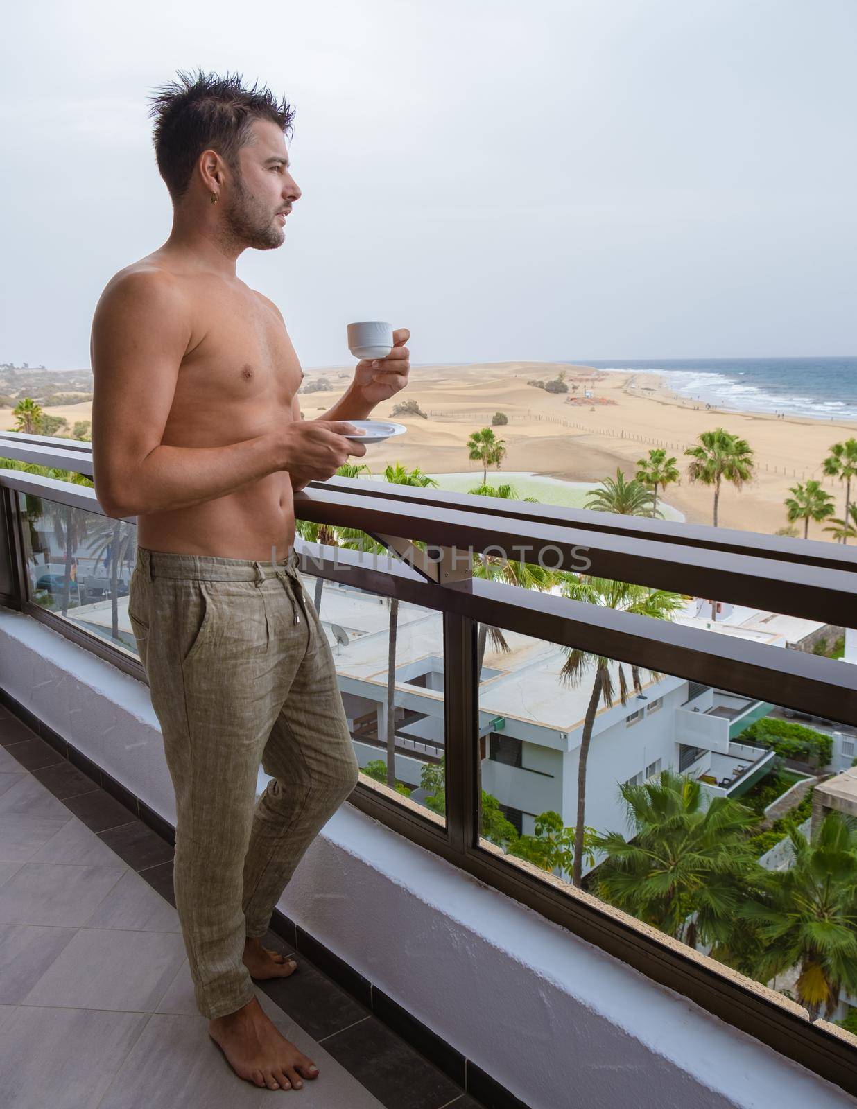 young men drinking coffee on the balcony during a vacation in Gran Canaria Spain. Young shirtless men looking out over the ocean