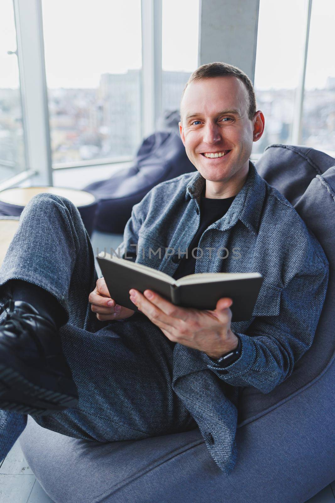 A male businessman in a casual suit resting in a comfortable pouf while working, an attractive freelancer in a suit works remotely and checks notes in a notebook