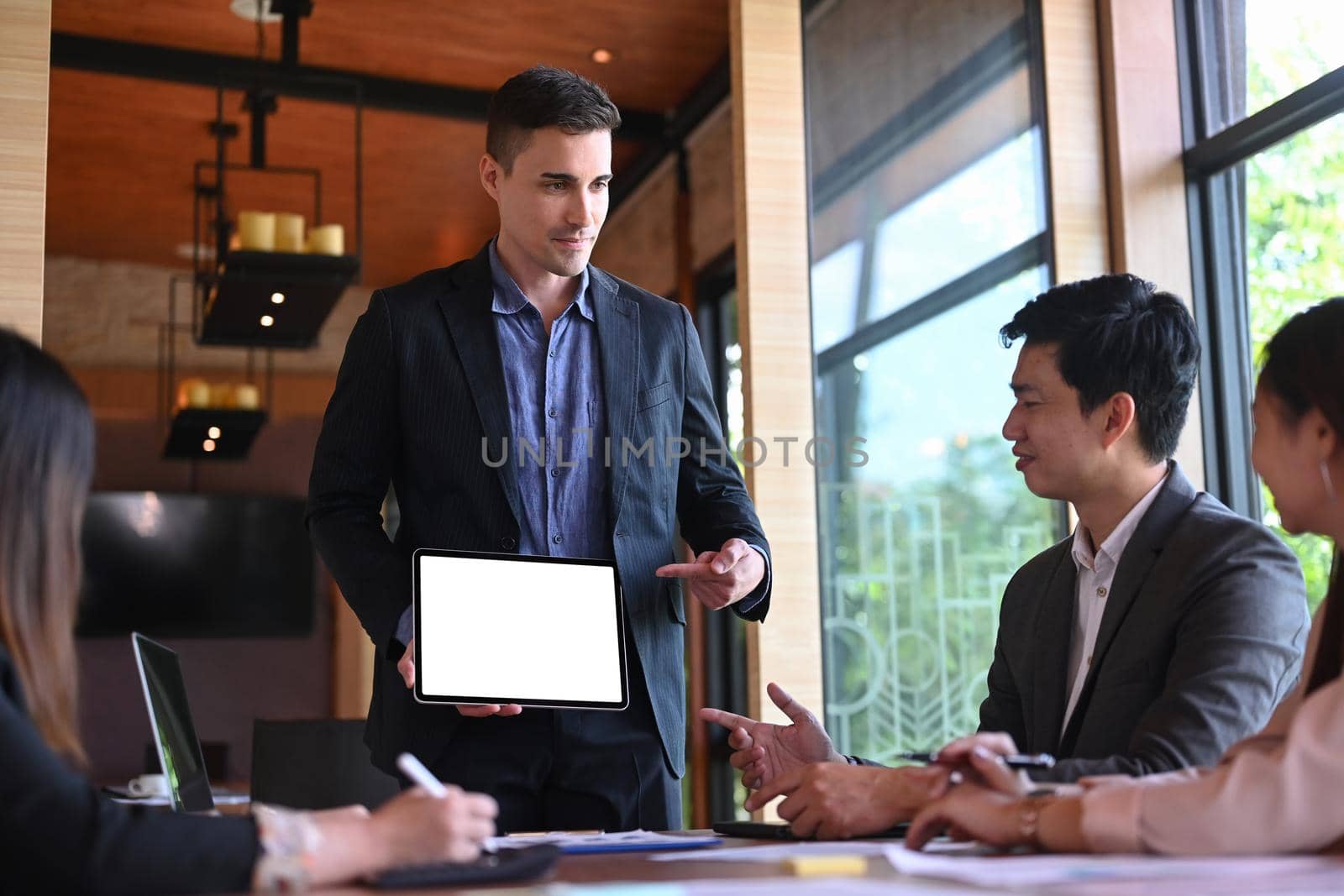 Handsome businessman presenting golding digital tablet and financial data to colleagues.