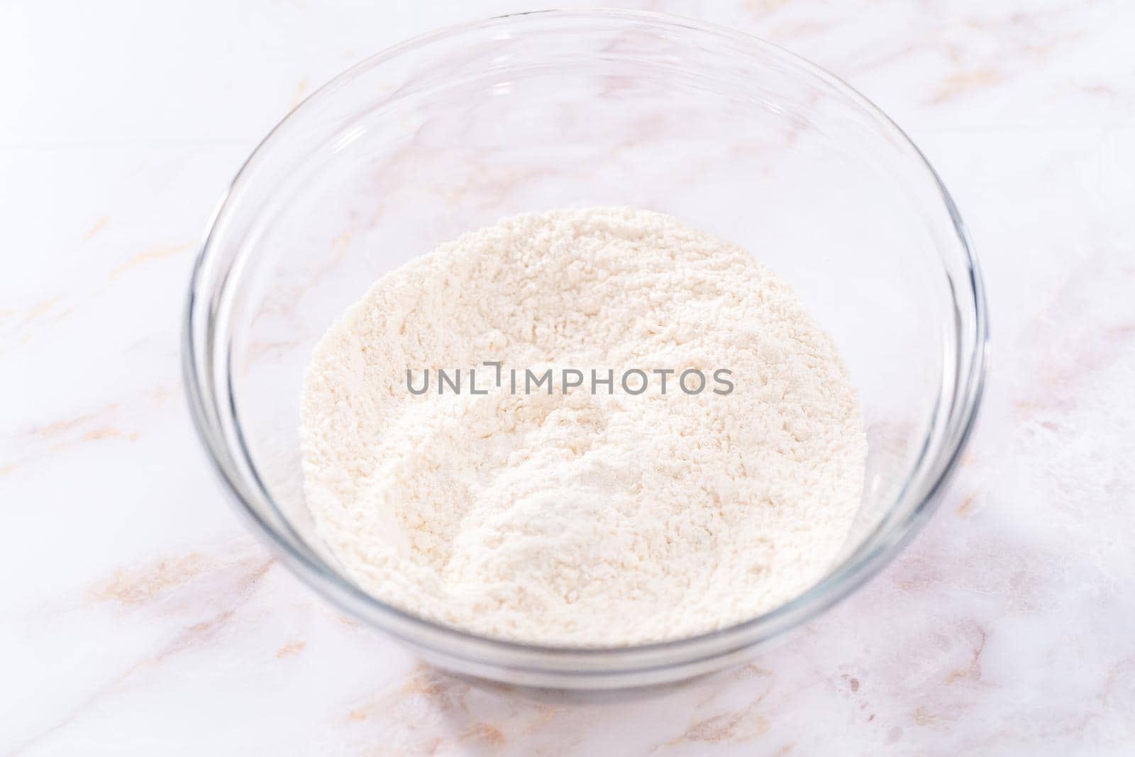 Mixing ingredients in a large glass mixing bowl to bake apple sharlotka muffin.