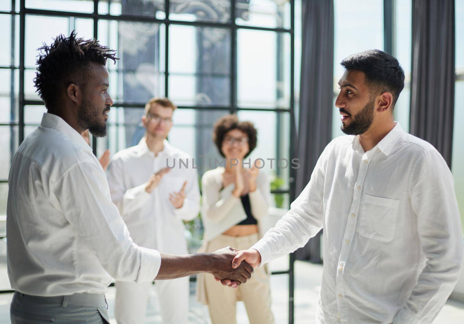 Glad to work with you. Young modern men in smart casual wear shaking hands and smiling while working in the creative office