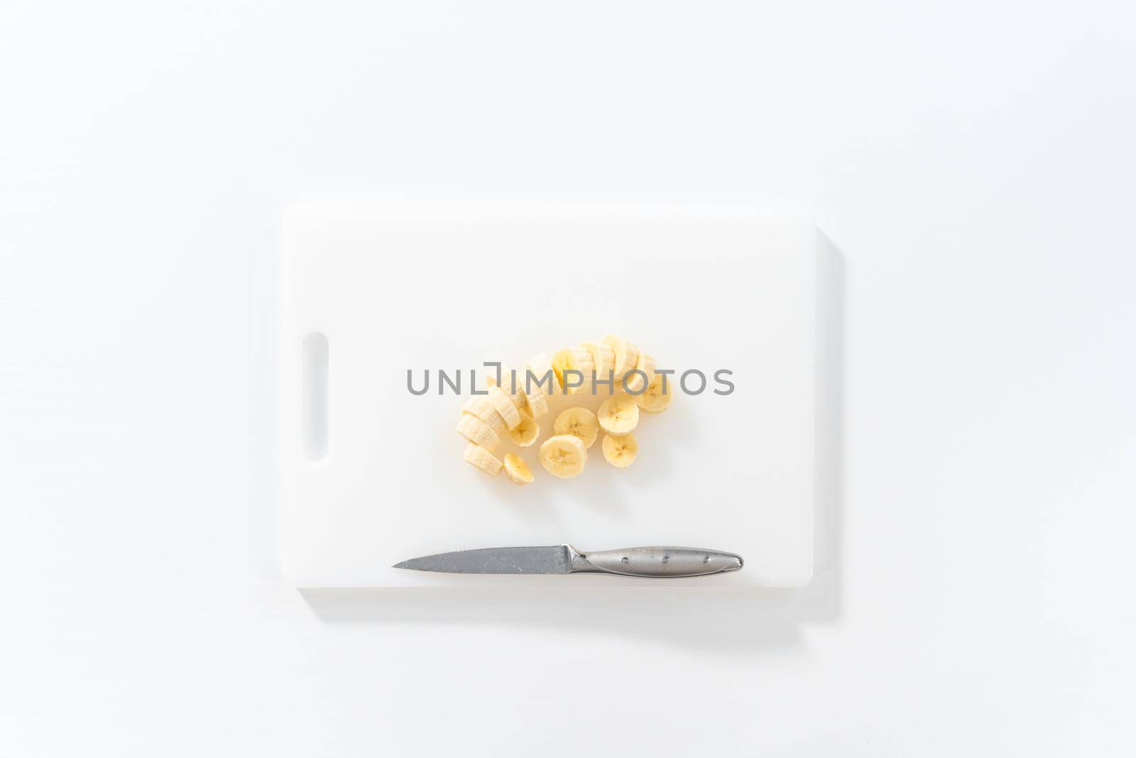 Flat lay. Slicing riped banana on a white cutting board.