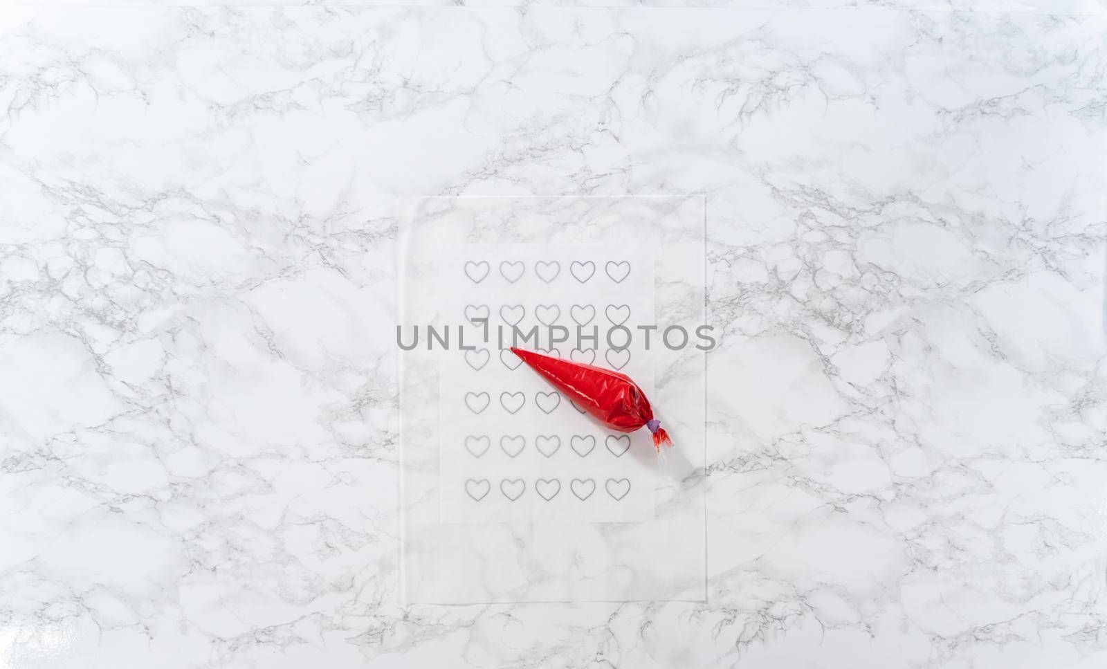 Flat lay. Piping melted chocolate from piping back over the parchment paper to make a chocolate heart.