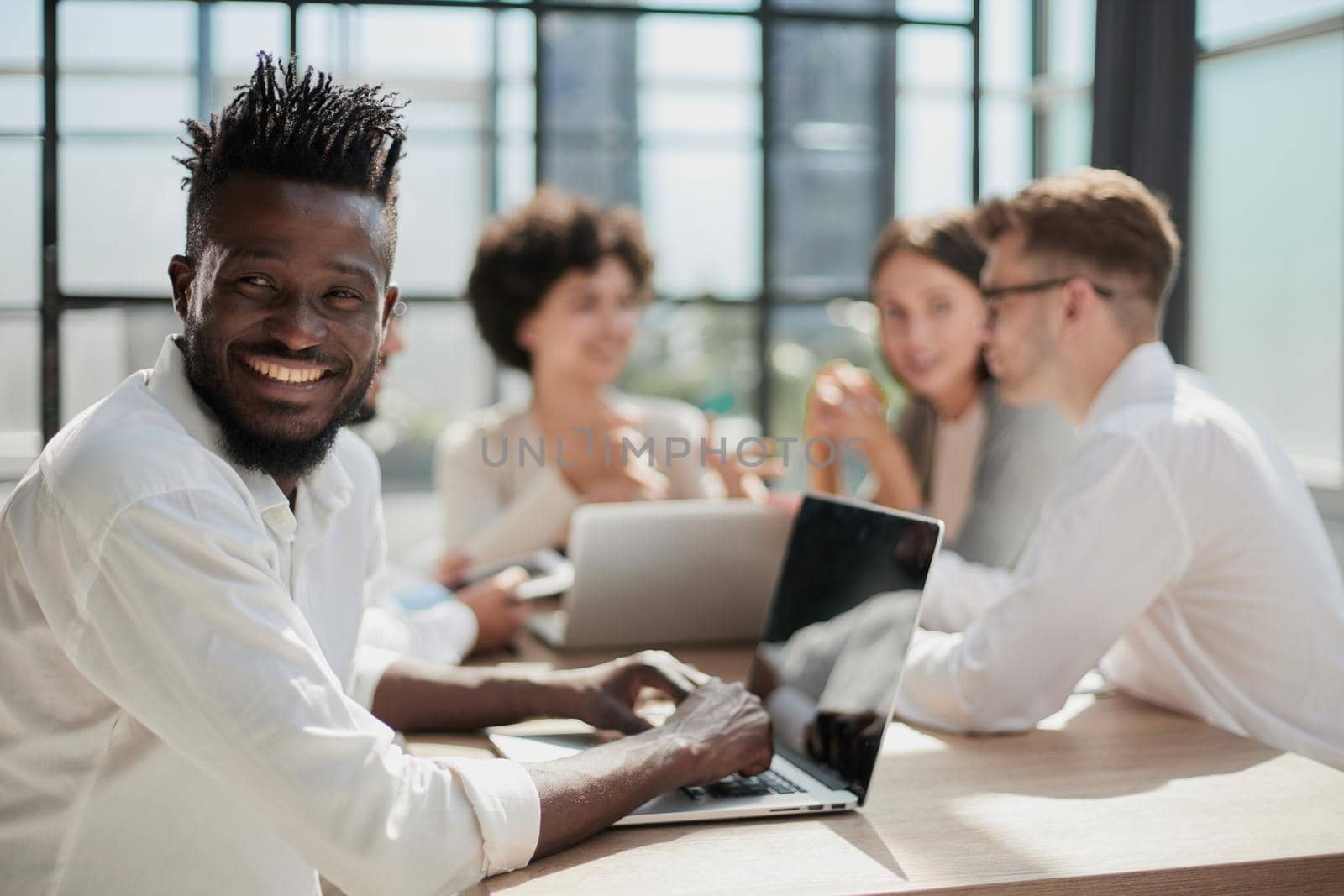 Portrait of smiling African American business man with executives working on laptop in background.