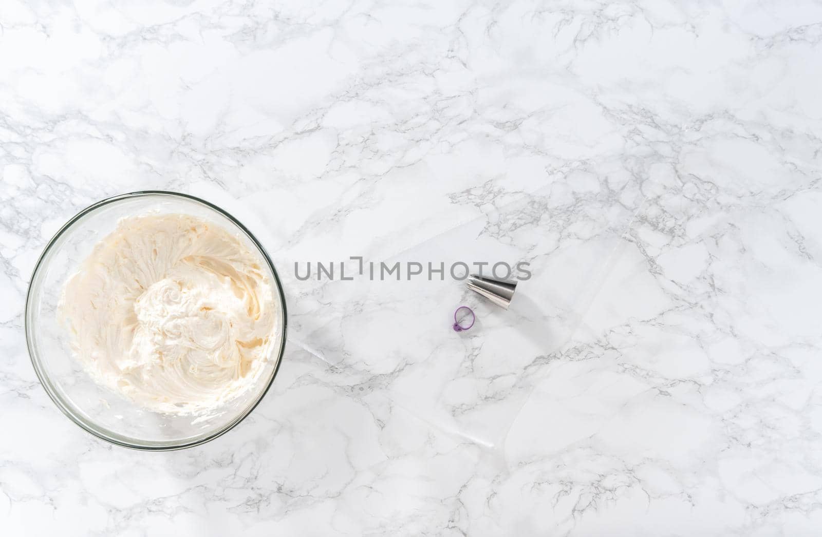 Flat lay. Whisking buttercream frosting in a glass mixing bowl with an electric hand mixer to prepare the peppermint buttercream frosting.