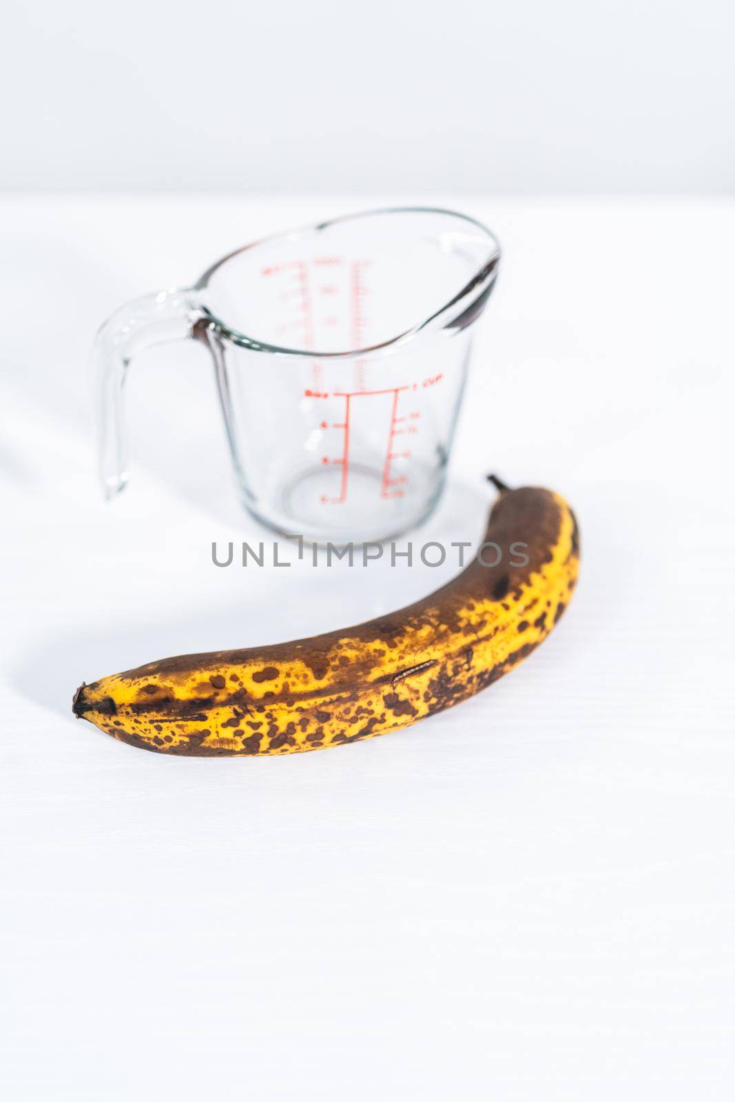 Riped and overripe bananas with a glass measuring cup on a white kitchen counter.