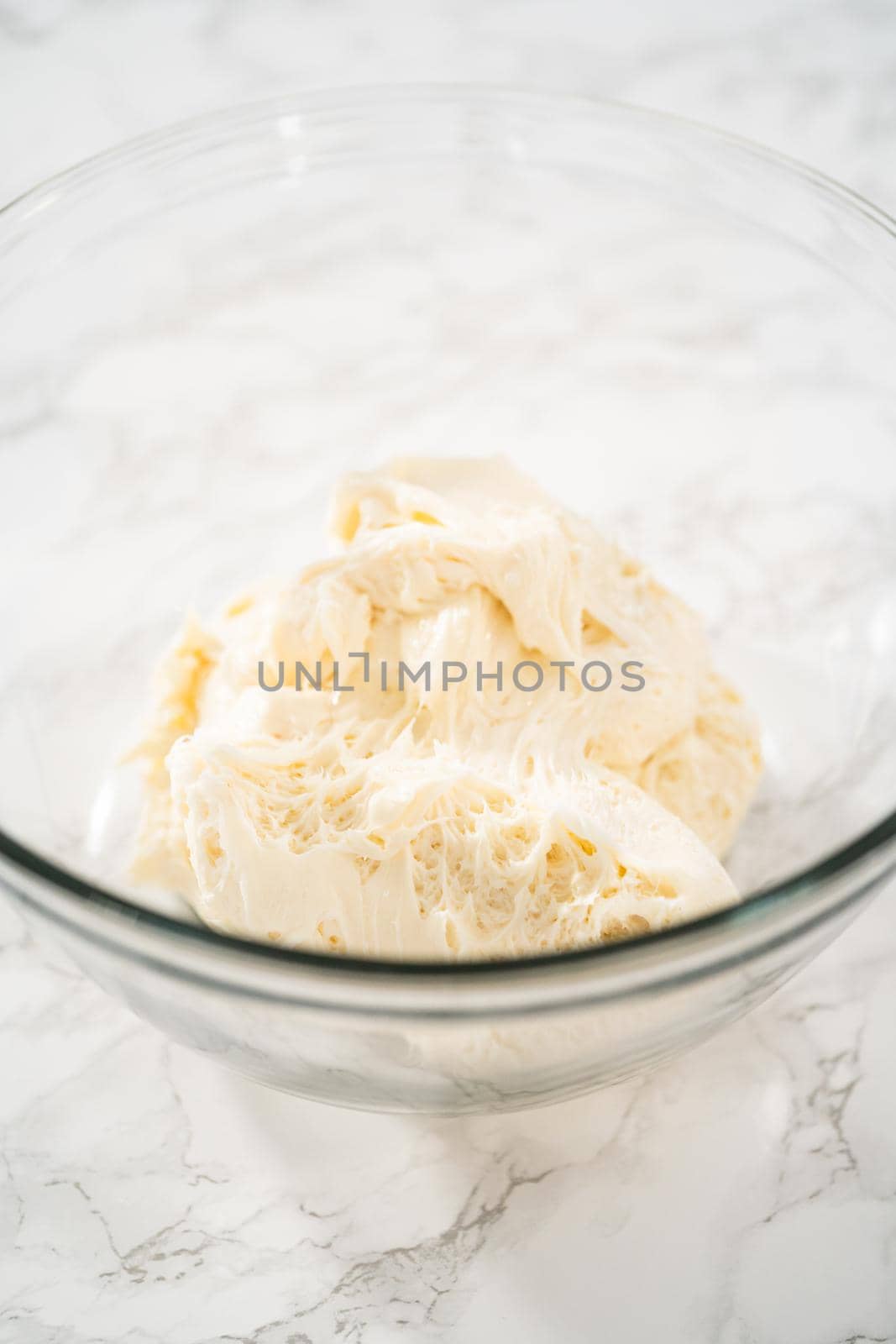 Whisking buttercream frosting in a glass mixing bowl with an electric hand mixer to prepare the peppermint buttercream frosting.
