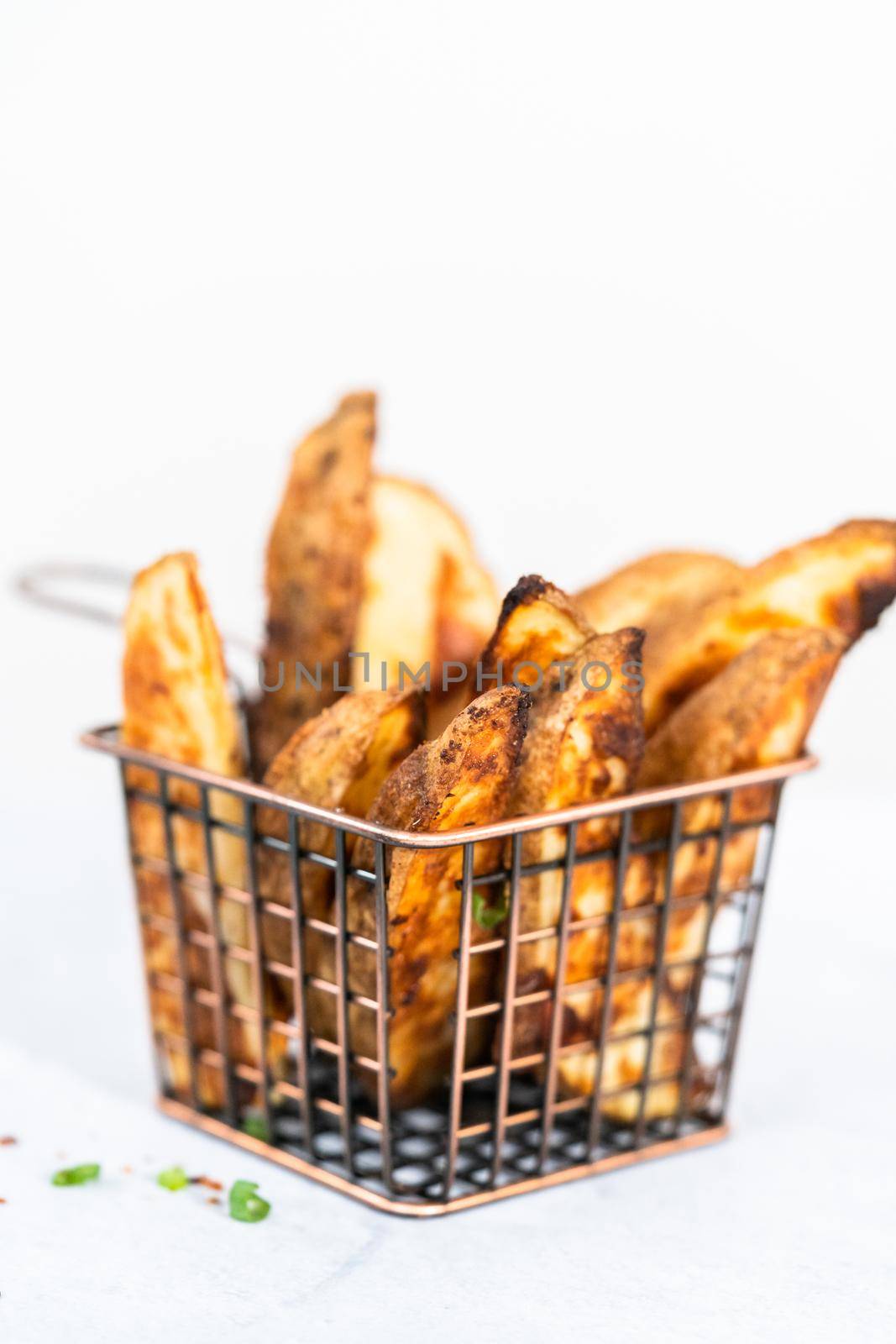 Freshly baked potato wedges with spices in a wire basket.