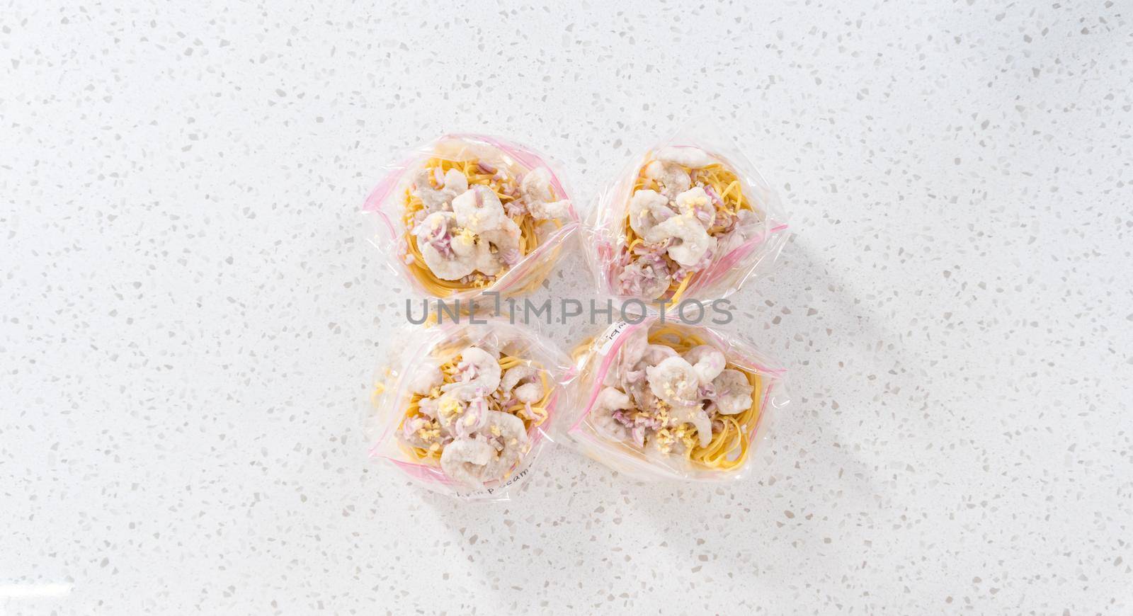 Flat lay. Packaging homemade frozen shrimp scampi meal prep into plastic resealable bags.