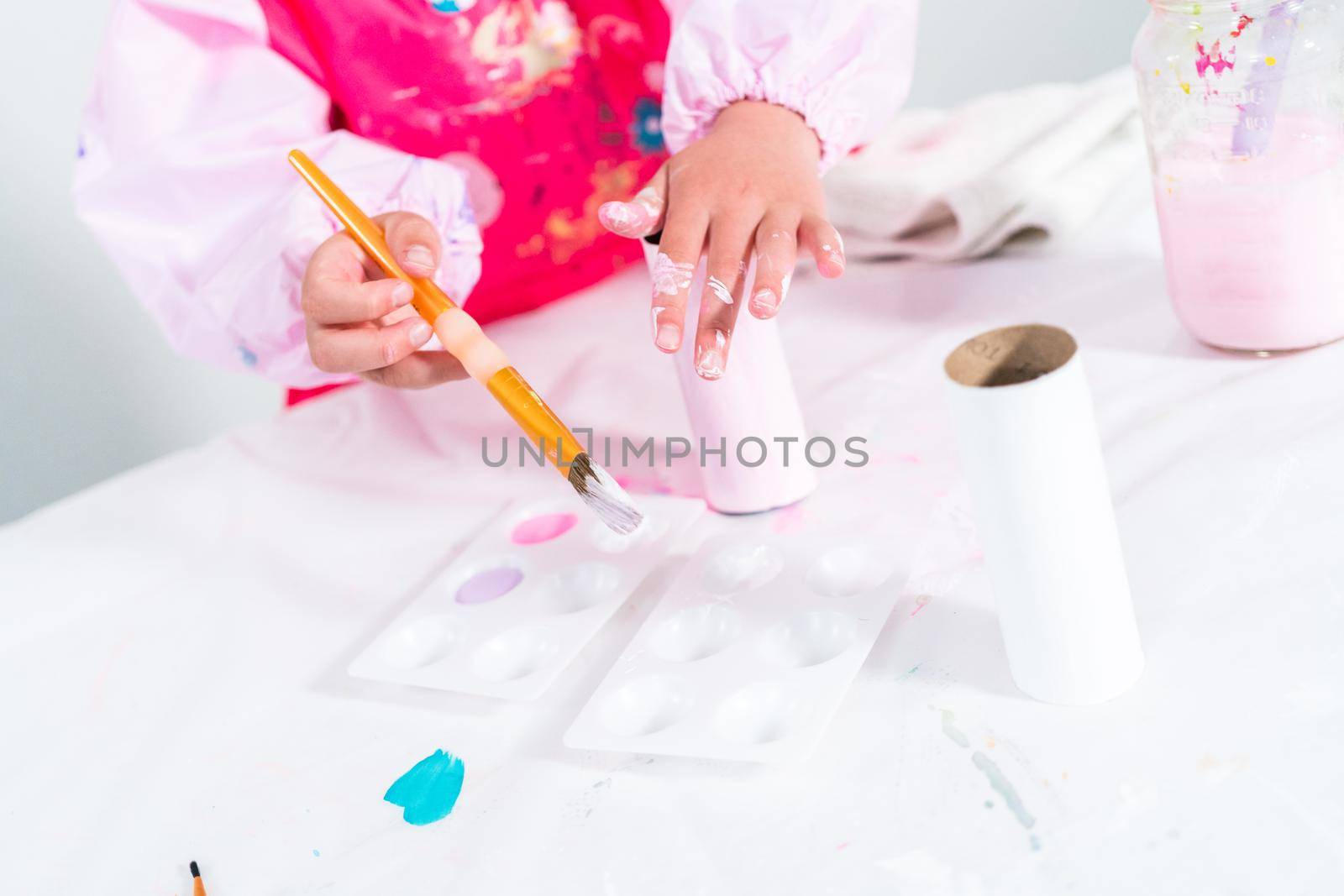 Little girl making a unicorn out of the toilet paper roll and craft paper.