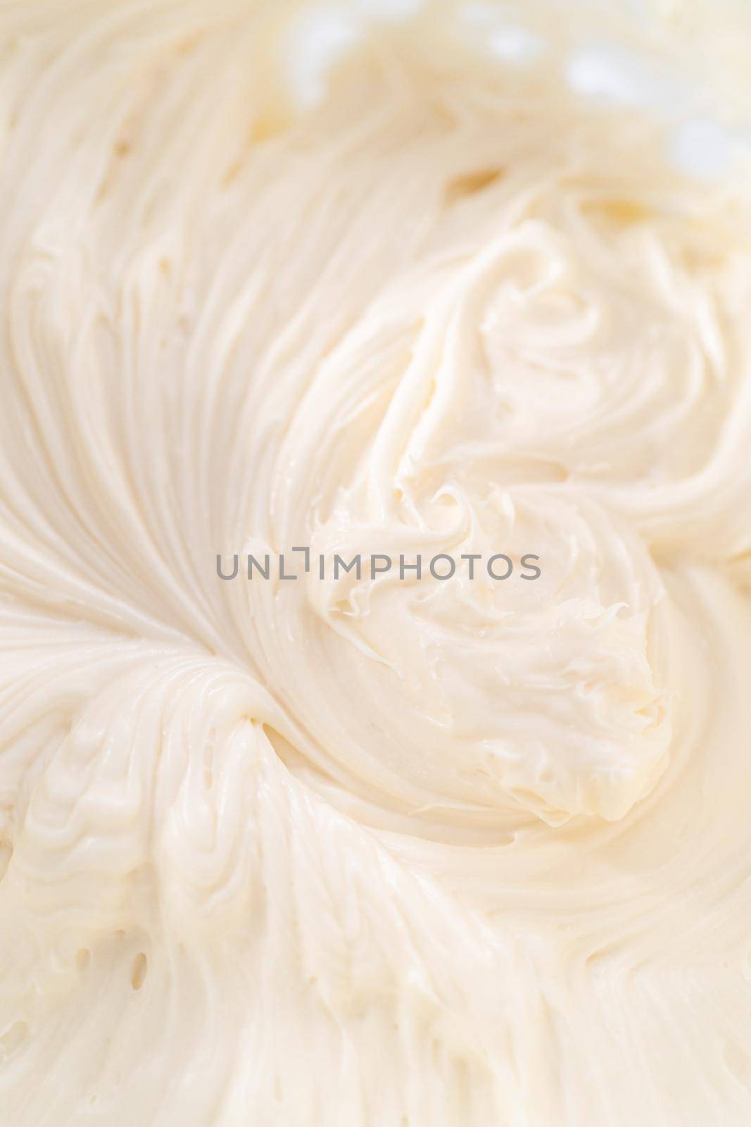 Mixing ingredients in a large glass mixing bowl to prepare cream cheese frosting.