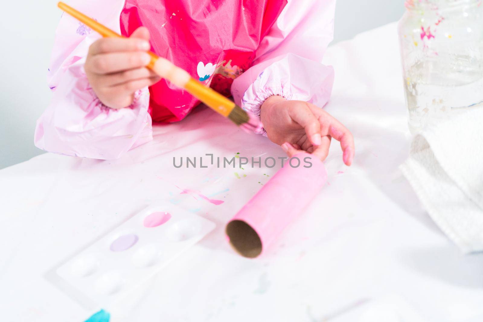 Little girl making a unicorn out of the toilet paper roll and craft paper.