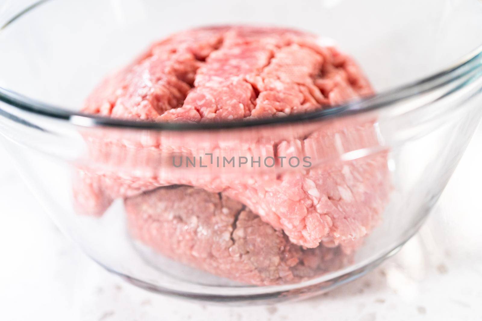 Mixing ingredients with a potatoe masher in a glass mixing bowl to prepare oven-baked meatballs.