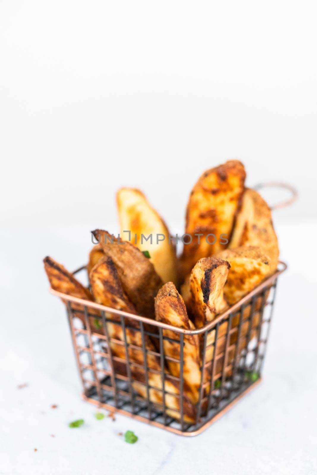 Freshly baked potato wedges with spices in a wire basket.