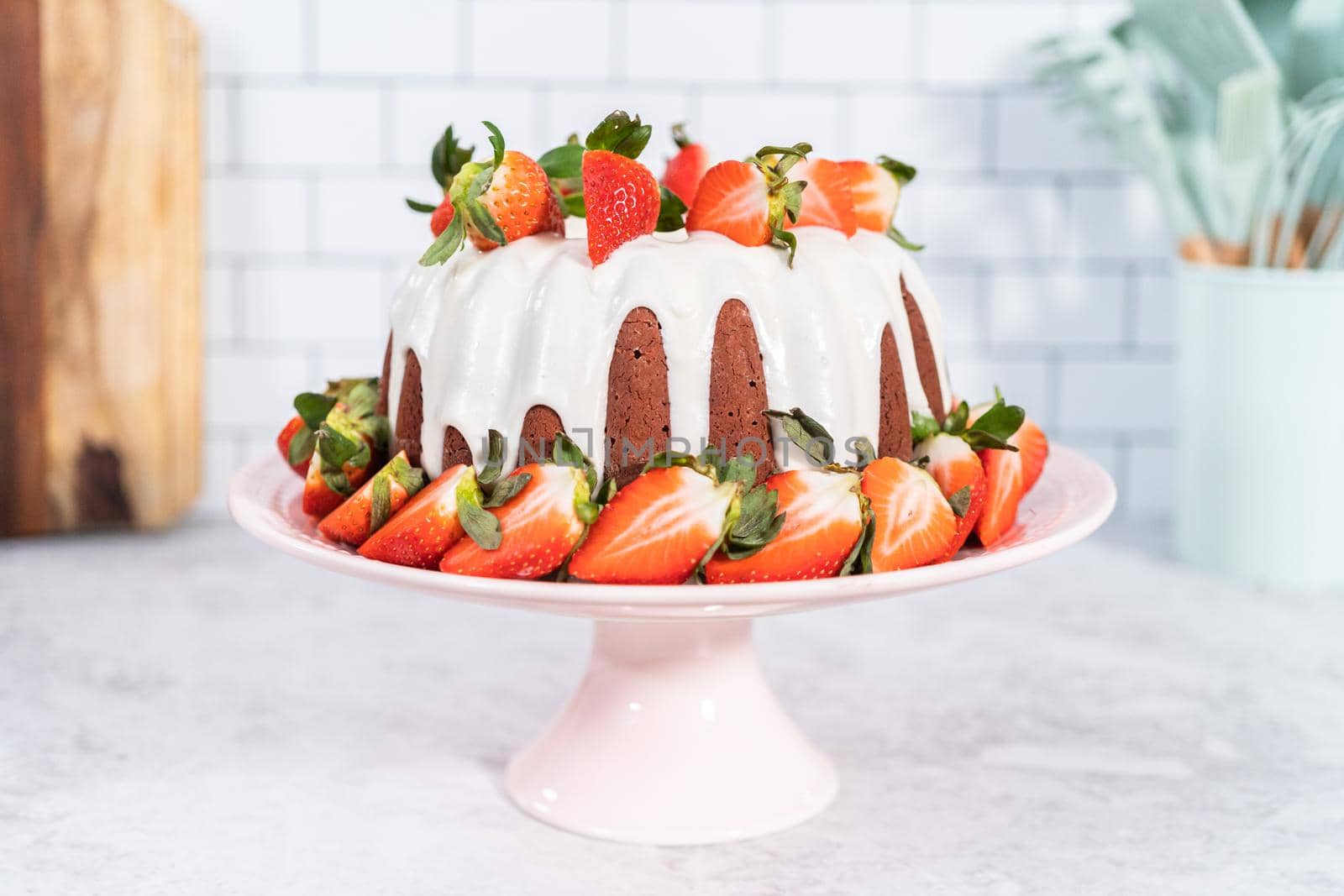 fresh strawberries..Red velvet bundt cake with cream cheese frosting garnished with fresh strawberries on a pink cake stand for Valentines Day.