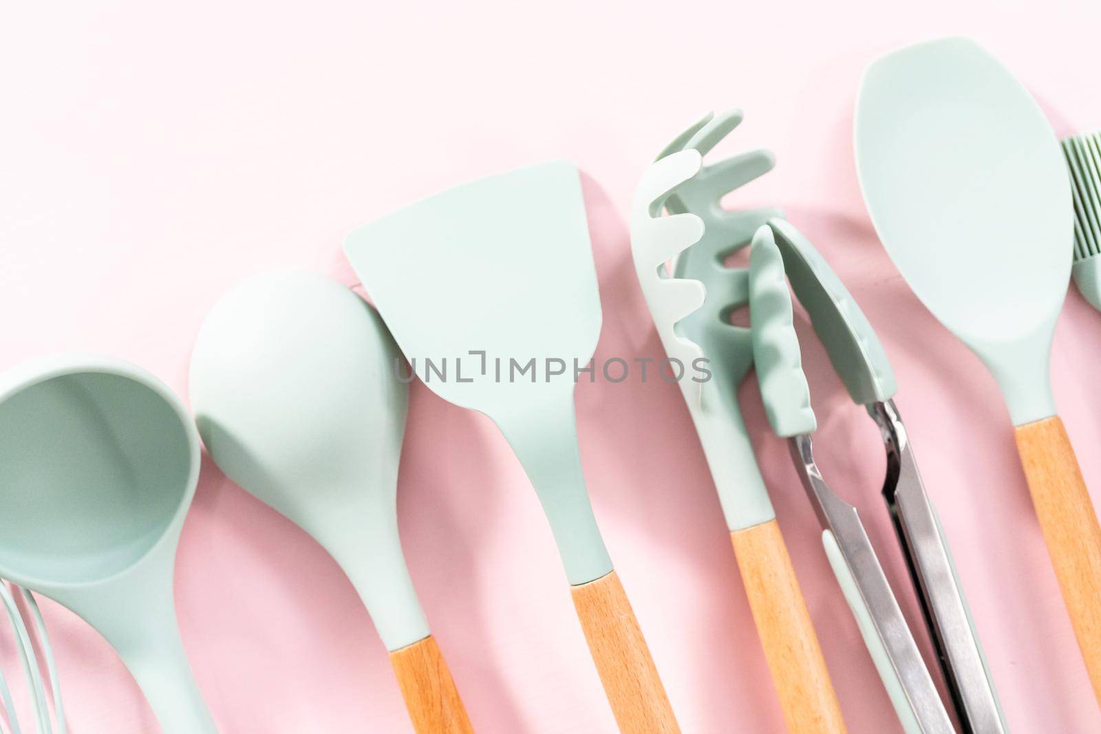 New blue silicone kitchen utensils with wooden handles on a pink background.