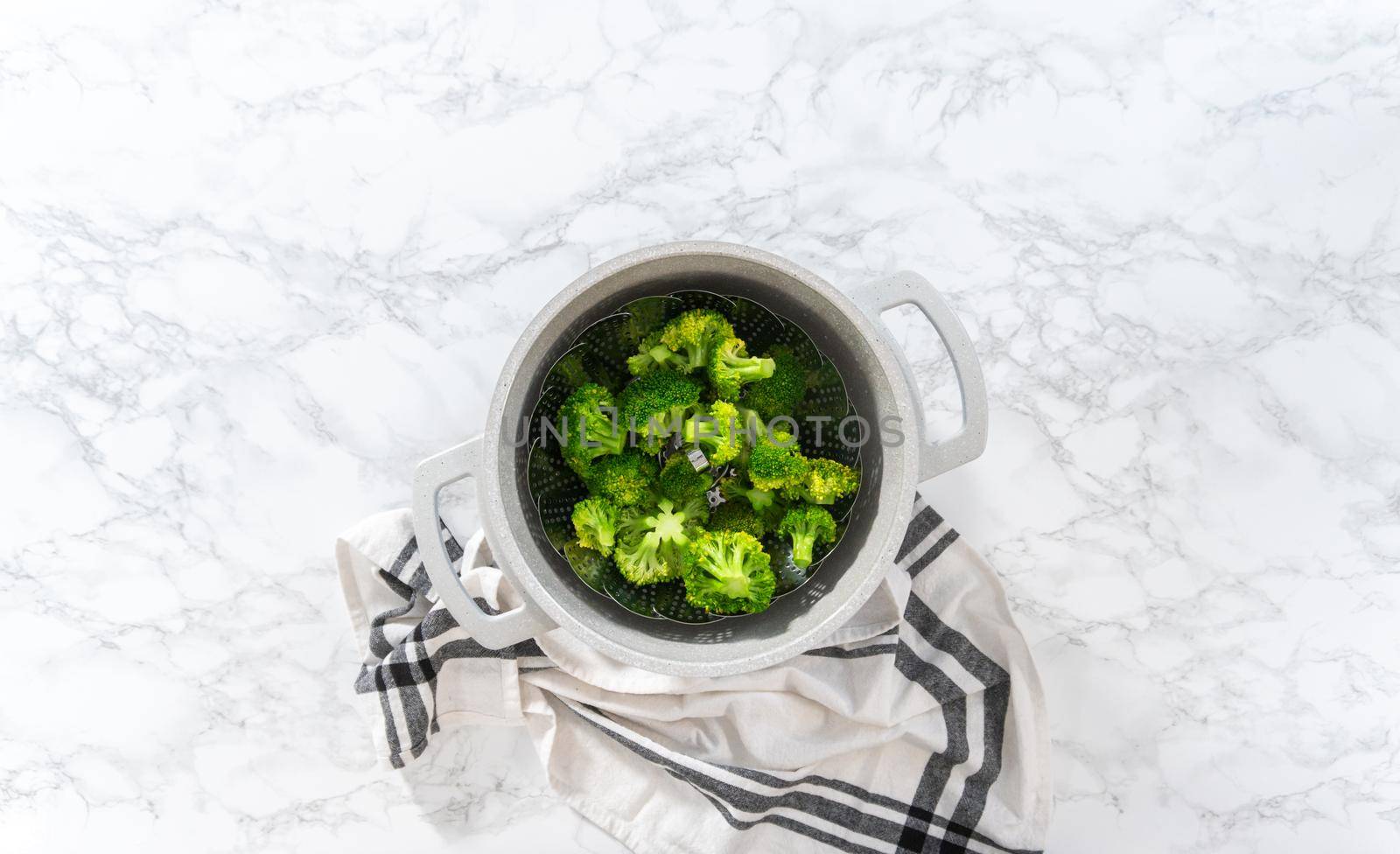 Flat lay. Steaming fresh broccoli in a cooking pot with a steamer basket to prepare steamed broccoli.