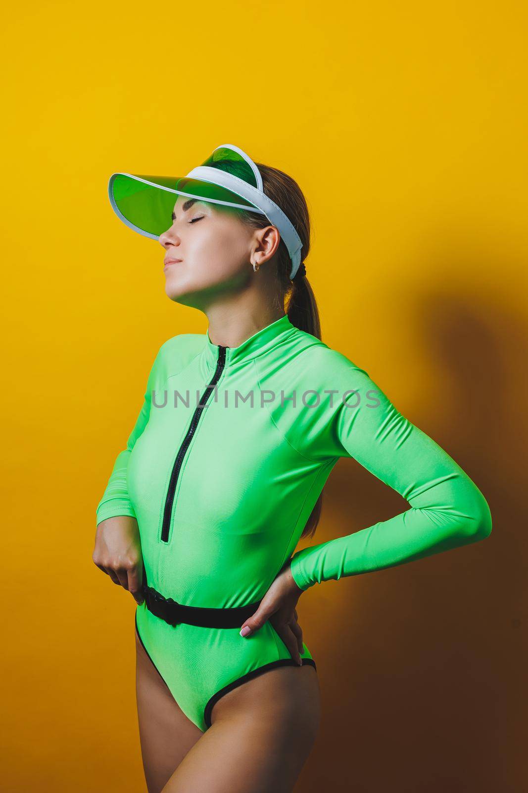 Attractive woman in bright green beach swimsuit, hat, on bright yellow background with perfect body. Isolated. Studio shot.