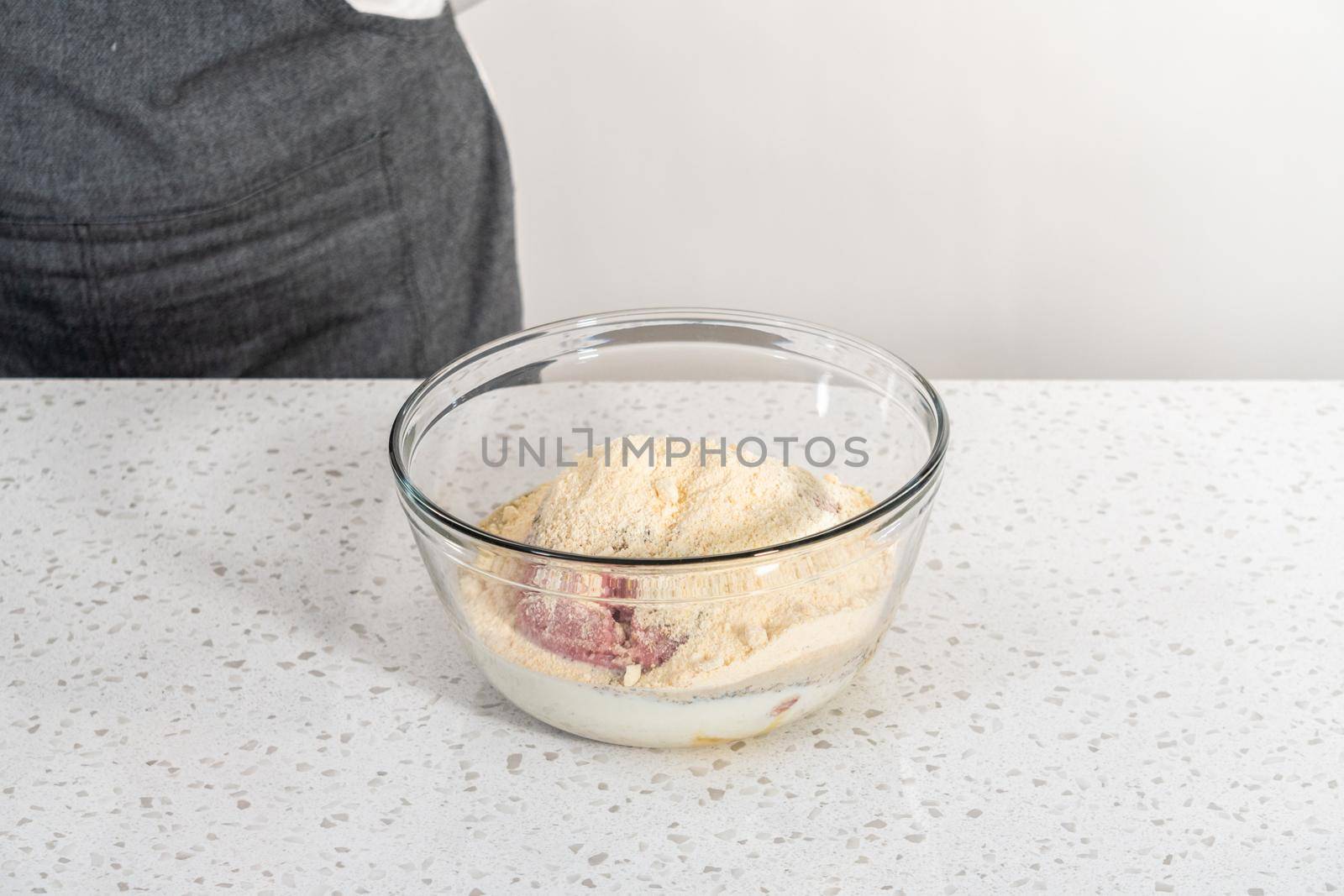 Mixing ingredients with a potatoe masher in a glass mixing bowl to prepare oven-baked meatballs.